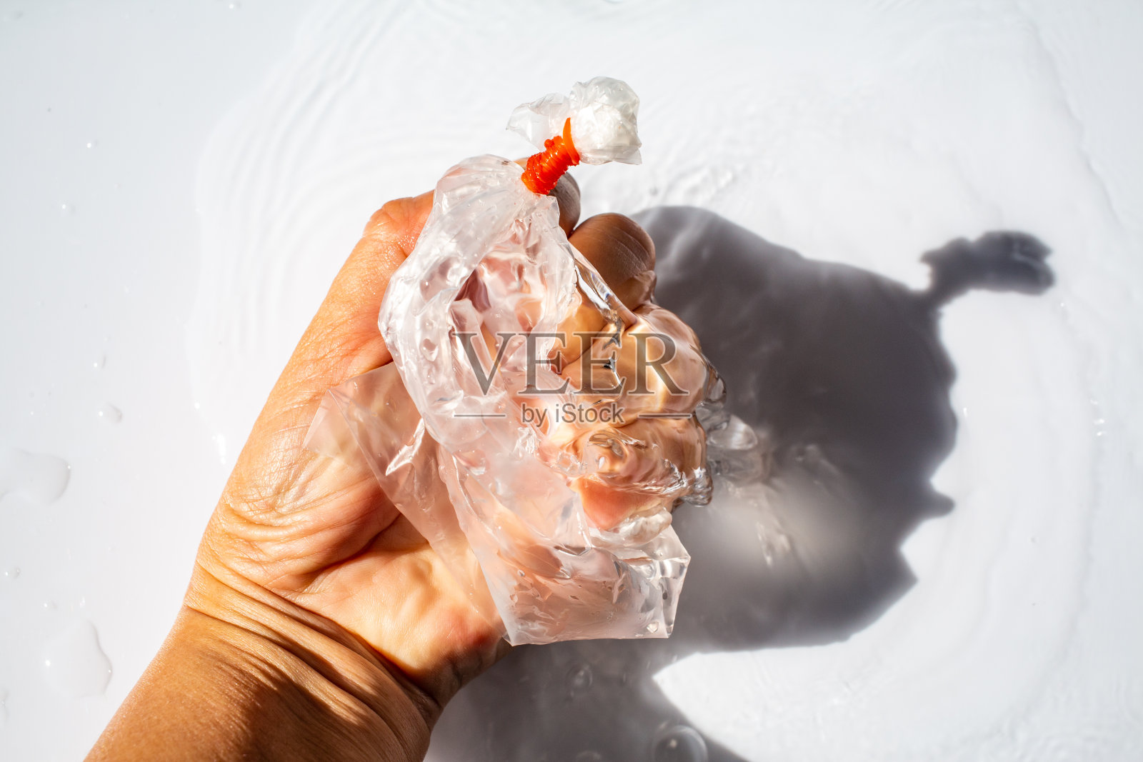 女人的手捏着装水的塑料袋，白色背景，光影照片摄影图片