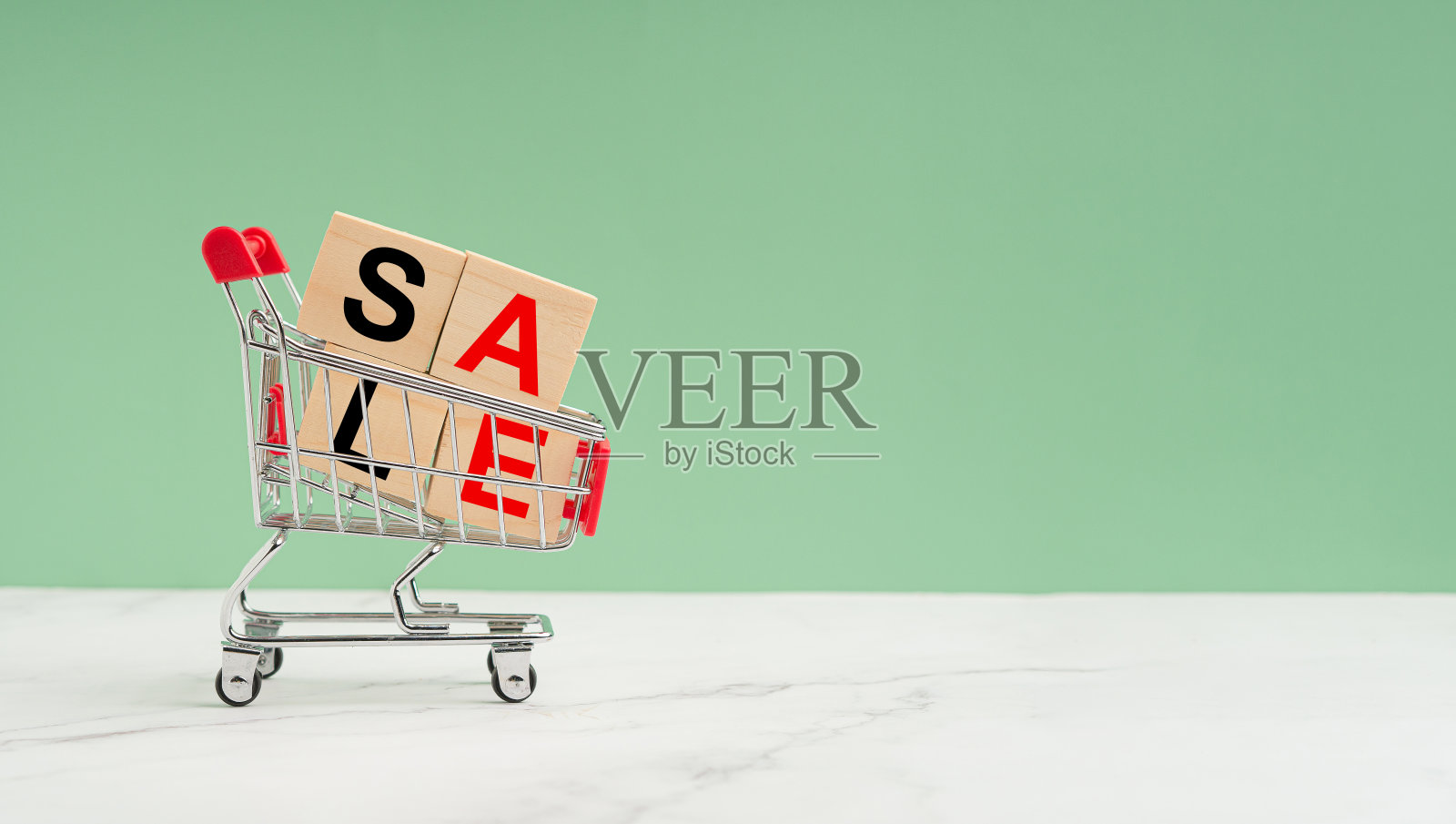 绿色背景的大理石地板上放着一辆迷你购物车和写着“SALE”字样的木块照片摄影图片