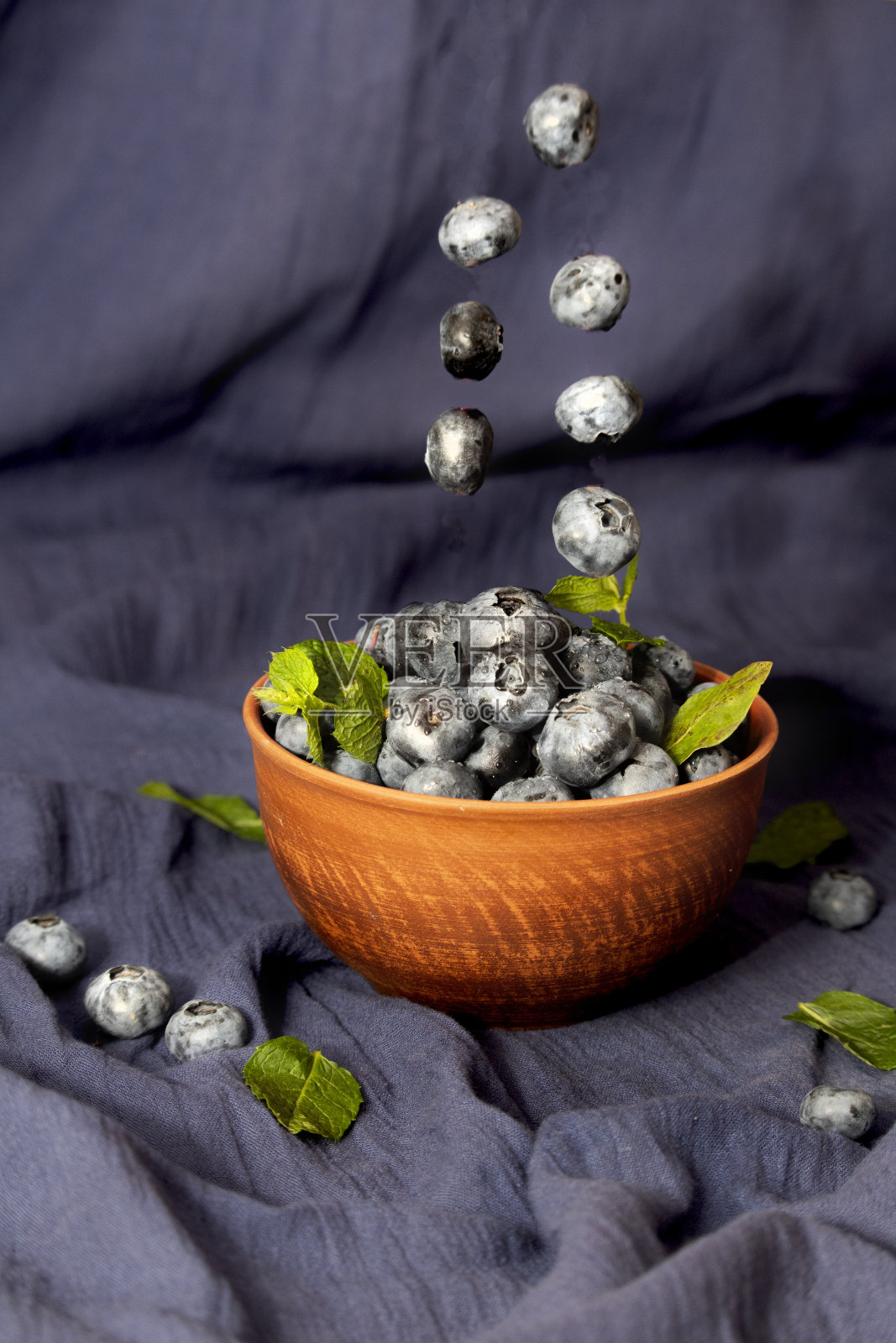 把新鲜蓝莓放在橙色陶瓷碗里，配上薄荷叶照片摄影图片