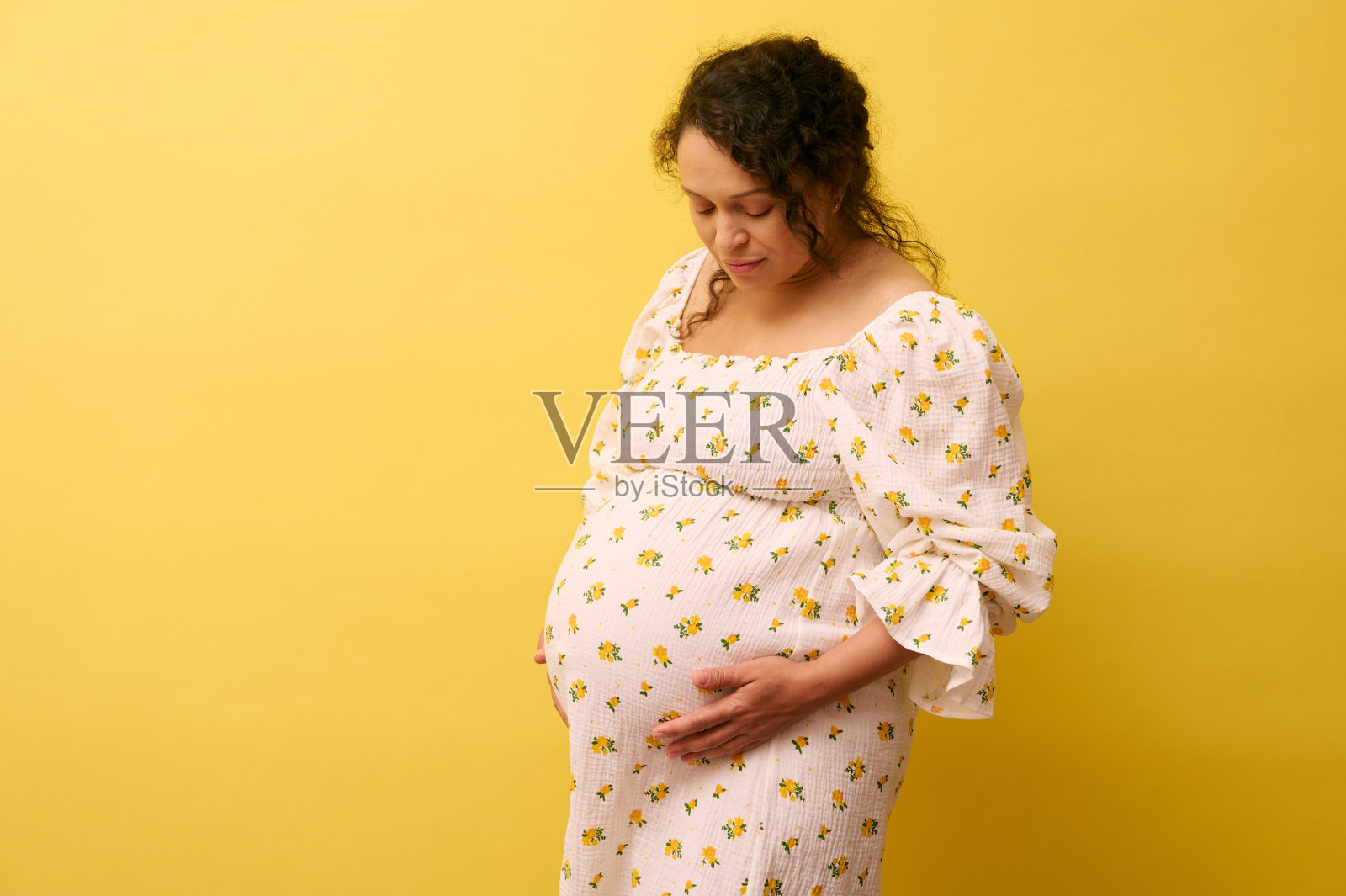 怀孕的女人轻轻地抚摸着她的大肚子在黄色的背景，复制空间。怀孕40周。生育观念照片摄影图片