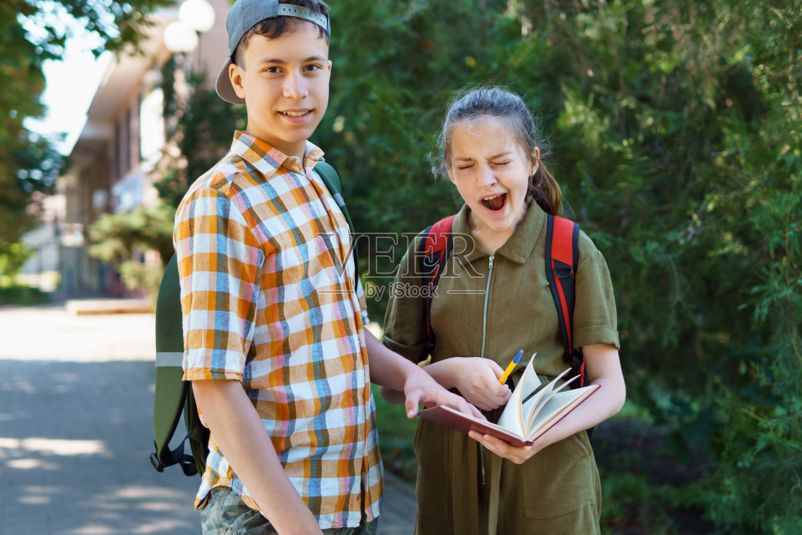 一个十几岁的男孩和一个十几岁的女孩正在打呵欠，厌倦了学习，想睡觉，夏日的城市街道照片摄影图片
