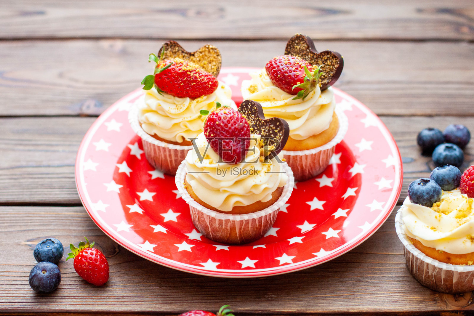 一套香草纸杯蛋糕，用新鲜的草莓，蓝莓，巧克力心和金色的点缀在红星盘上照片摄影图片