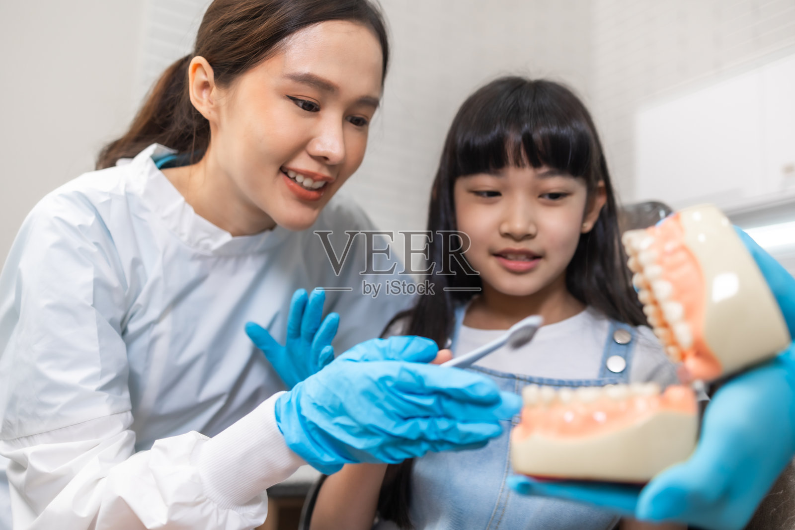 女牙医在牙科诊所拿着牙齿模型和孩子说话。照片摄影图片