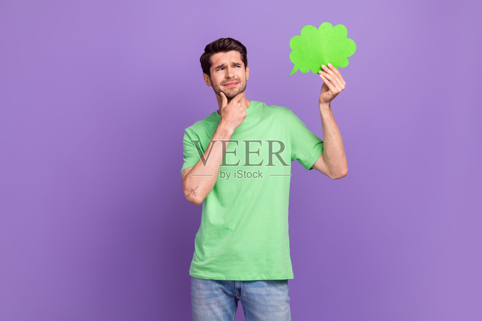 照片中聪明的男人穿着绿色t恤，手放在下巴上，若有所思地看着紫色背景上的空白空间照片摄影图片