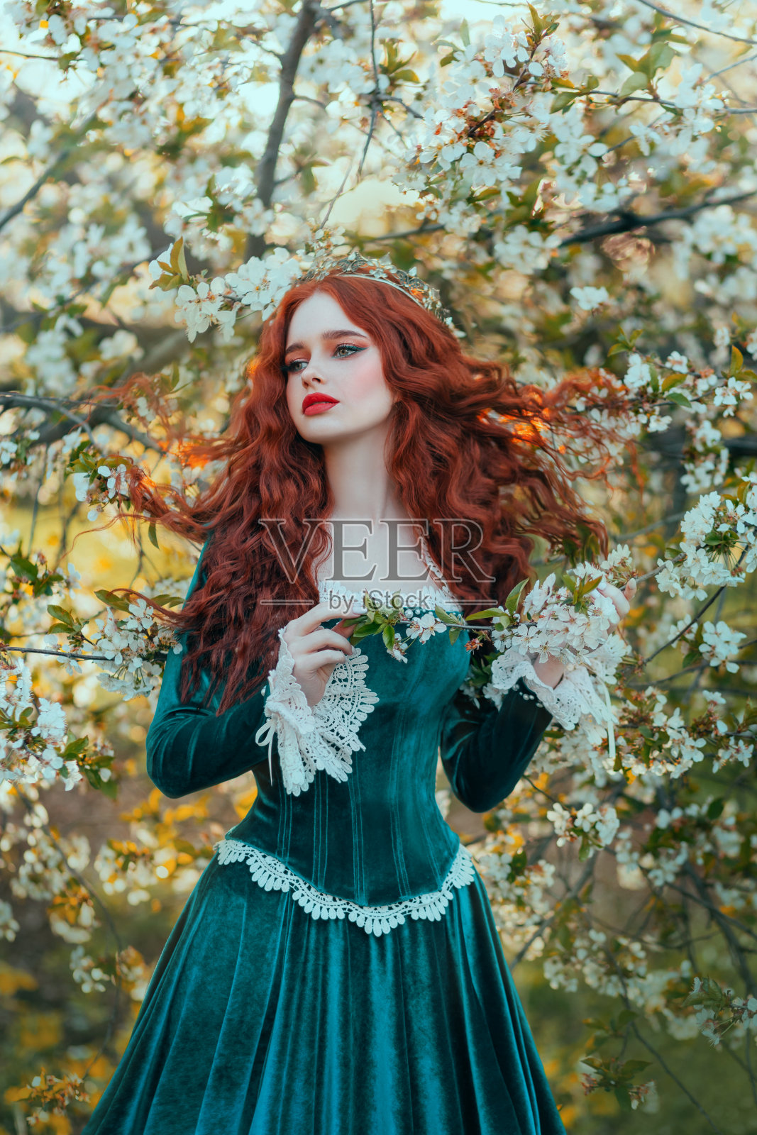 红发幻想女王。蓝色天鹅绒中世纪长裙，复古服装。红色的卷发随风飘扬。夏季自然，绿树开花，花园，小径，户外森林公园。行走的公主照片摄影图片