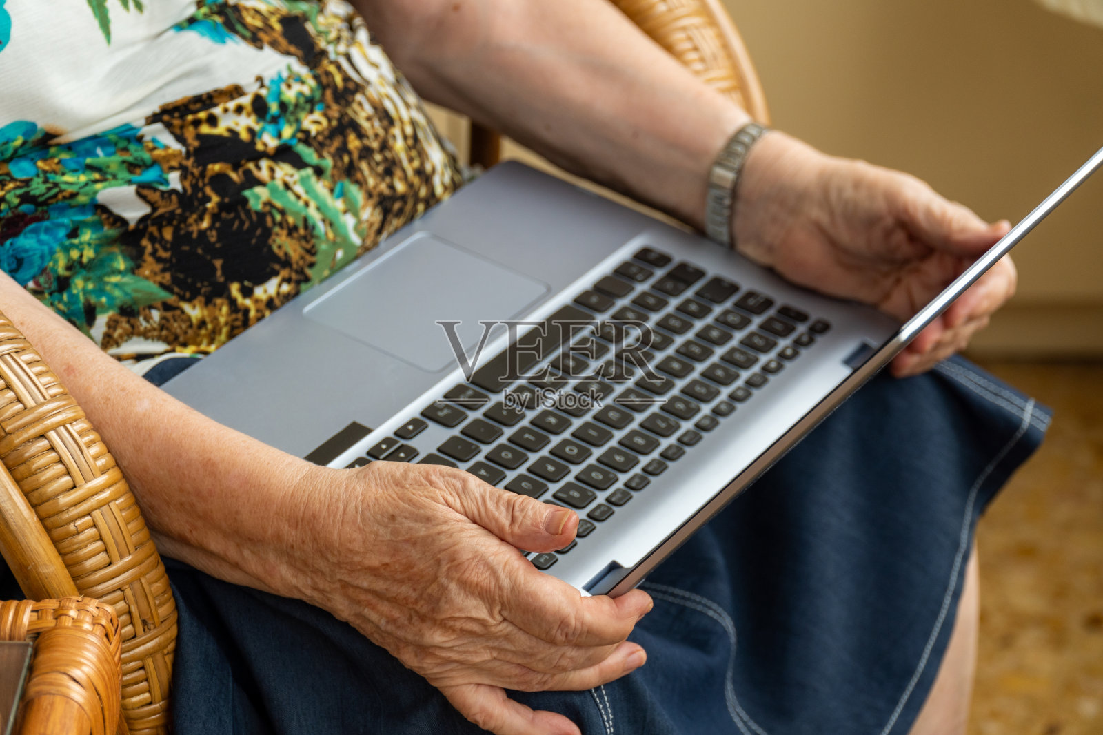 老年妇女双手拿着笔记本电脑，坐在家里的椅子上照片摄影图片
