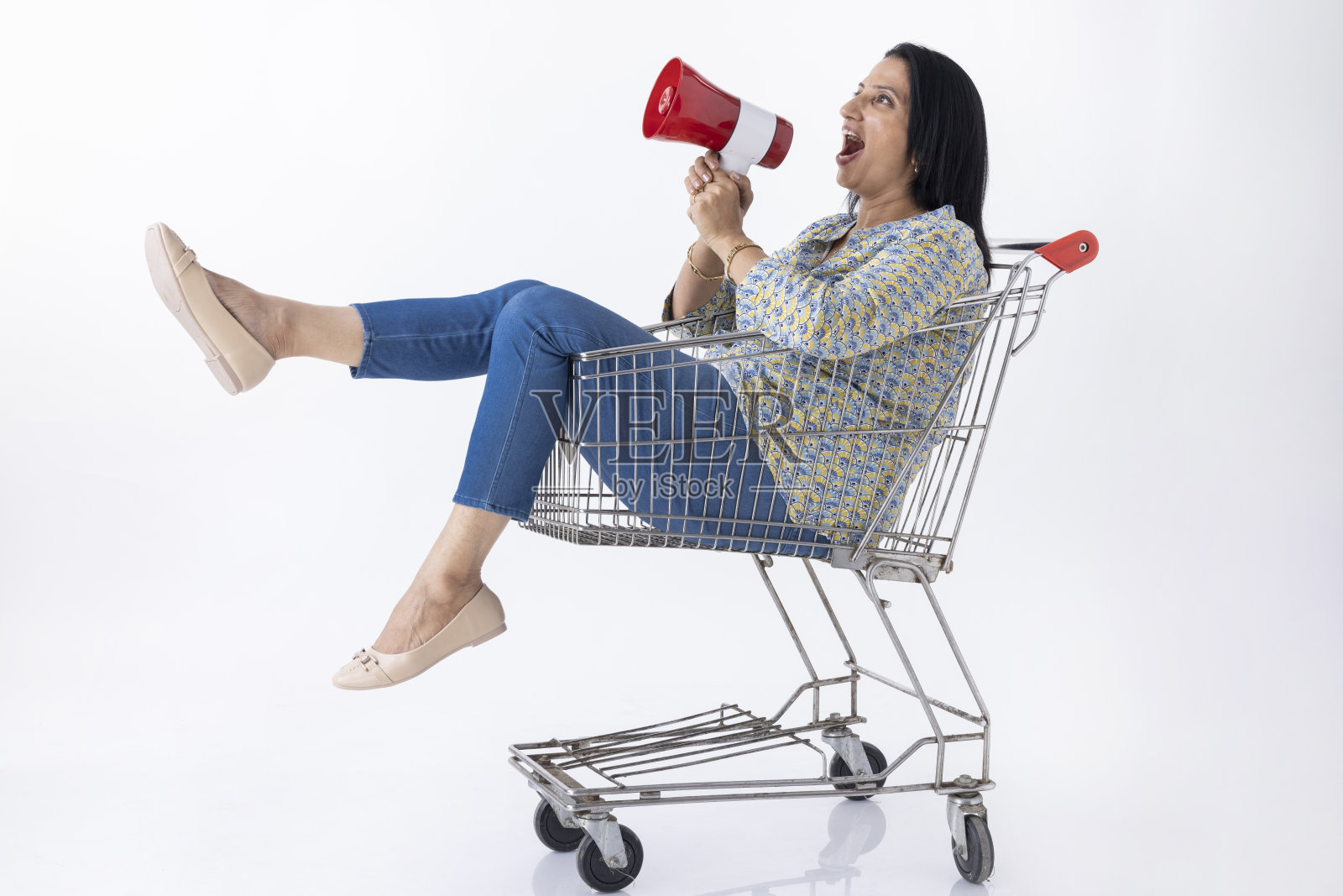 一名女子坐在购物车里，拿着扩音器，被隔离在白色背景中，照片摄影图片