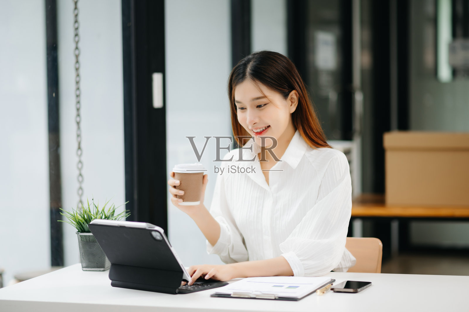 年轻漂亮的亚洲女人在平板电脑和笔记本电脑上打字，而坐在工作的白色桌子现代办公室照片摄影图片