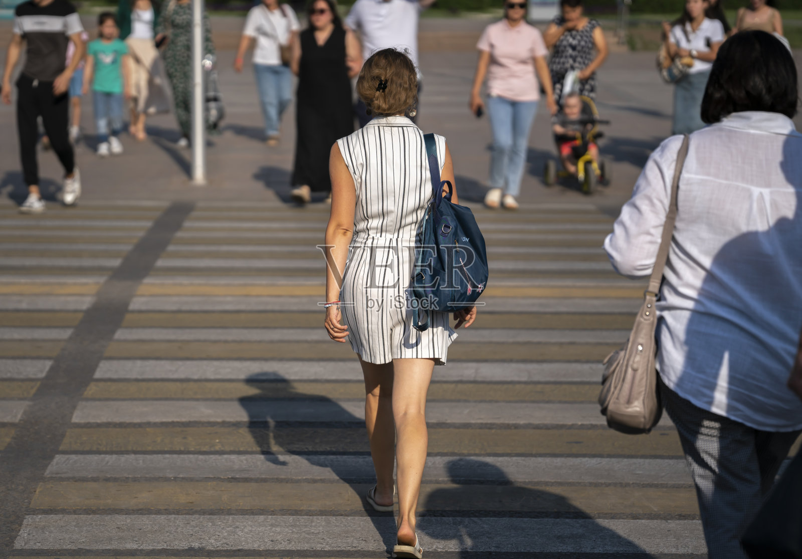 一位年轻的金发女子在市中心的人行横道上过马路。照片摄影图片