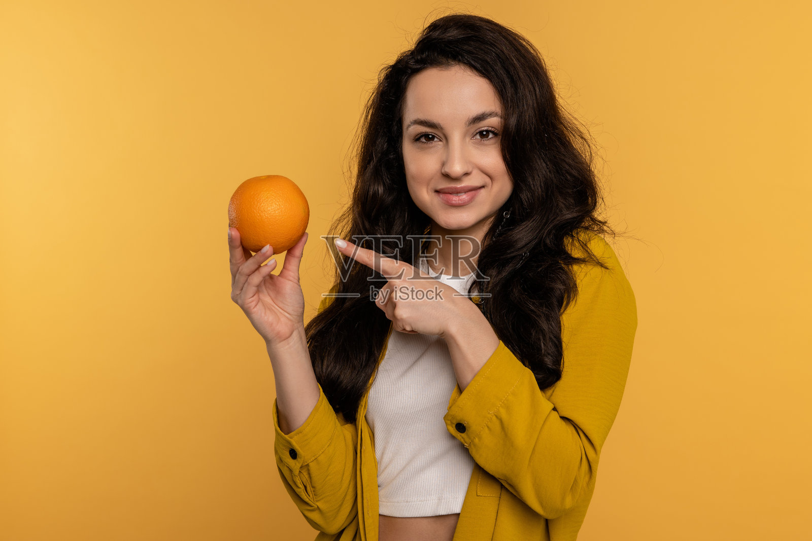 这位苗条的年轻女子在镜头前展示她最喜欢的柑橘类水果，背景是黄色的。健康食物概念照片摄影图片