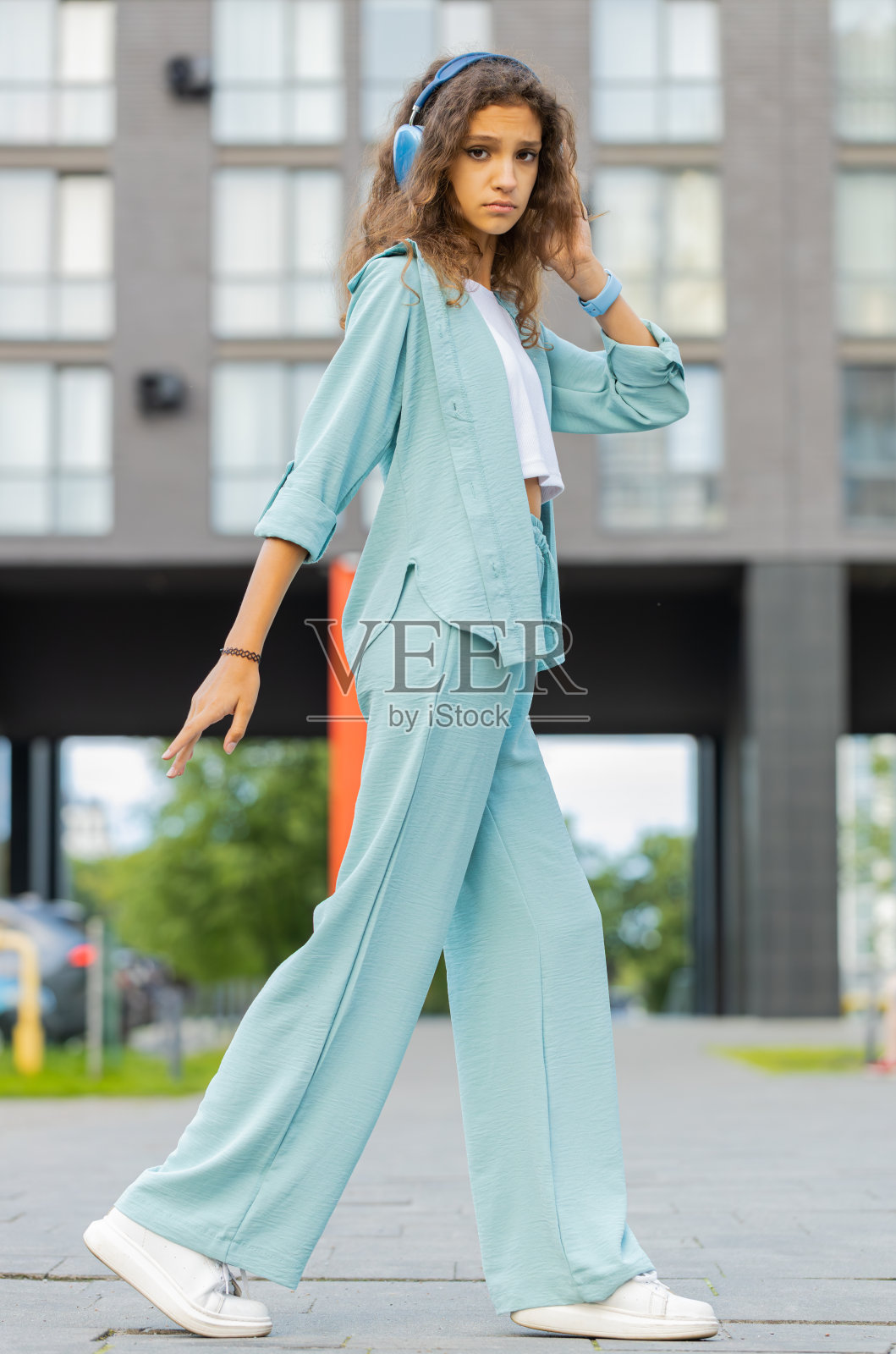 快乐的青春期前的孩子戴着无线耳机，听着音乐，在户外跳舞，走在城市的街道上照片摄影图片