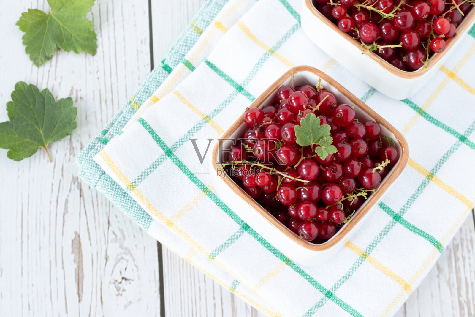 木桌上的碗里盛着新鲜的红加仑子和绿叶，俯视图照片摄影图片