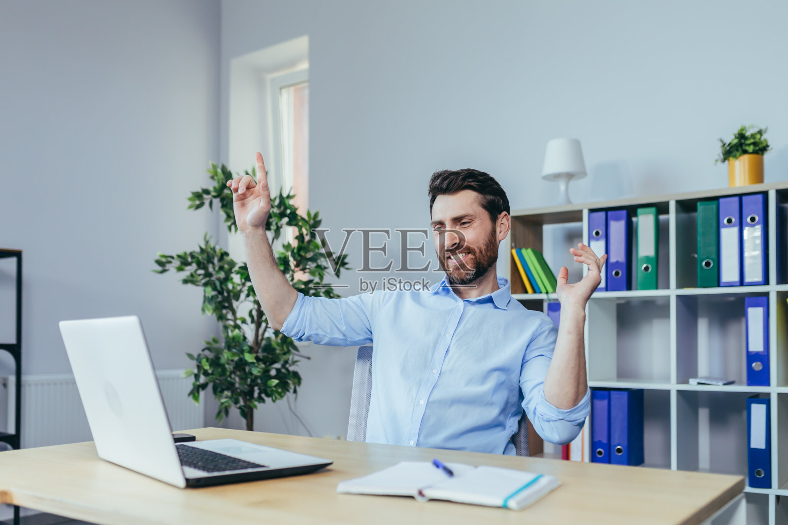 一个商人在明亮的办公室里工作，在桌子旁用笔记本电脑跳舞庆祝成功照片摄影图片