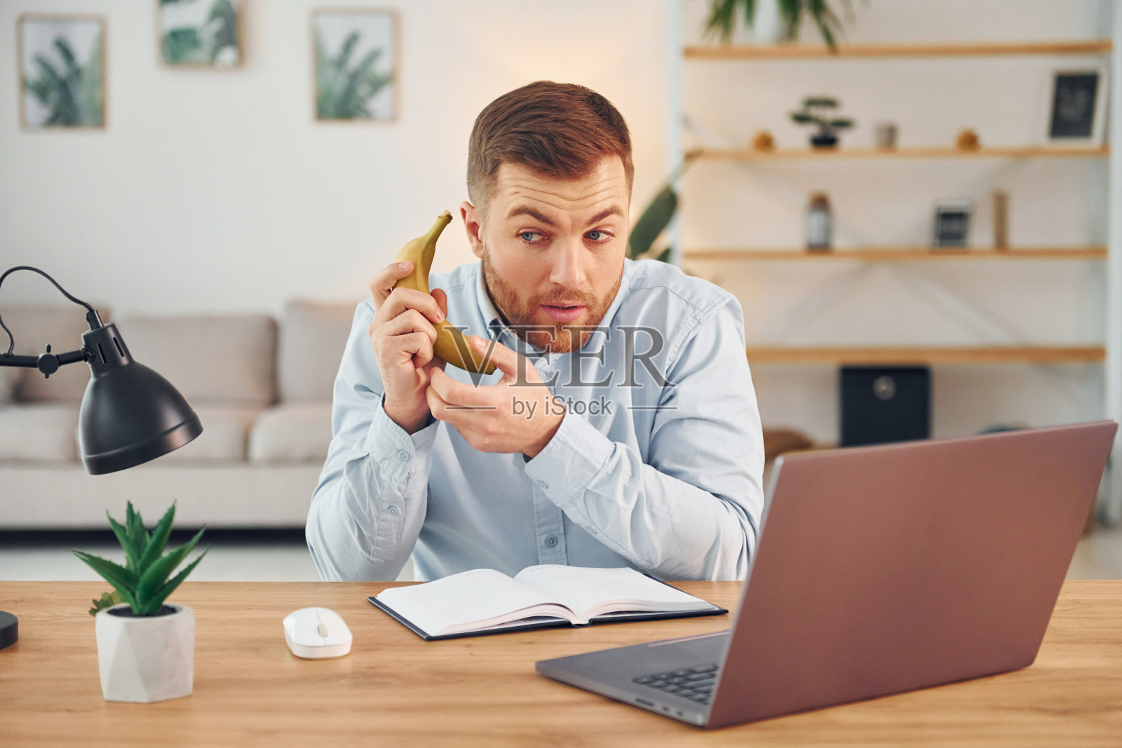 拿着水果。拿着香蕉的男人坐在桌子旁，笔记本电脑放在上面，玩得开心照片摄影图片