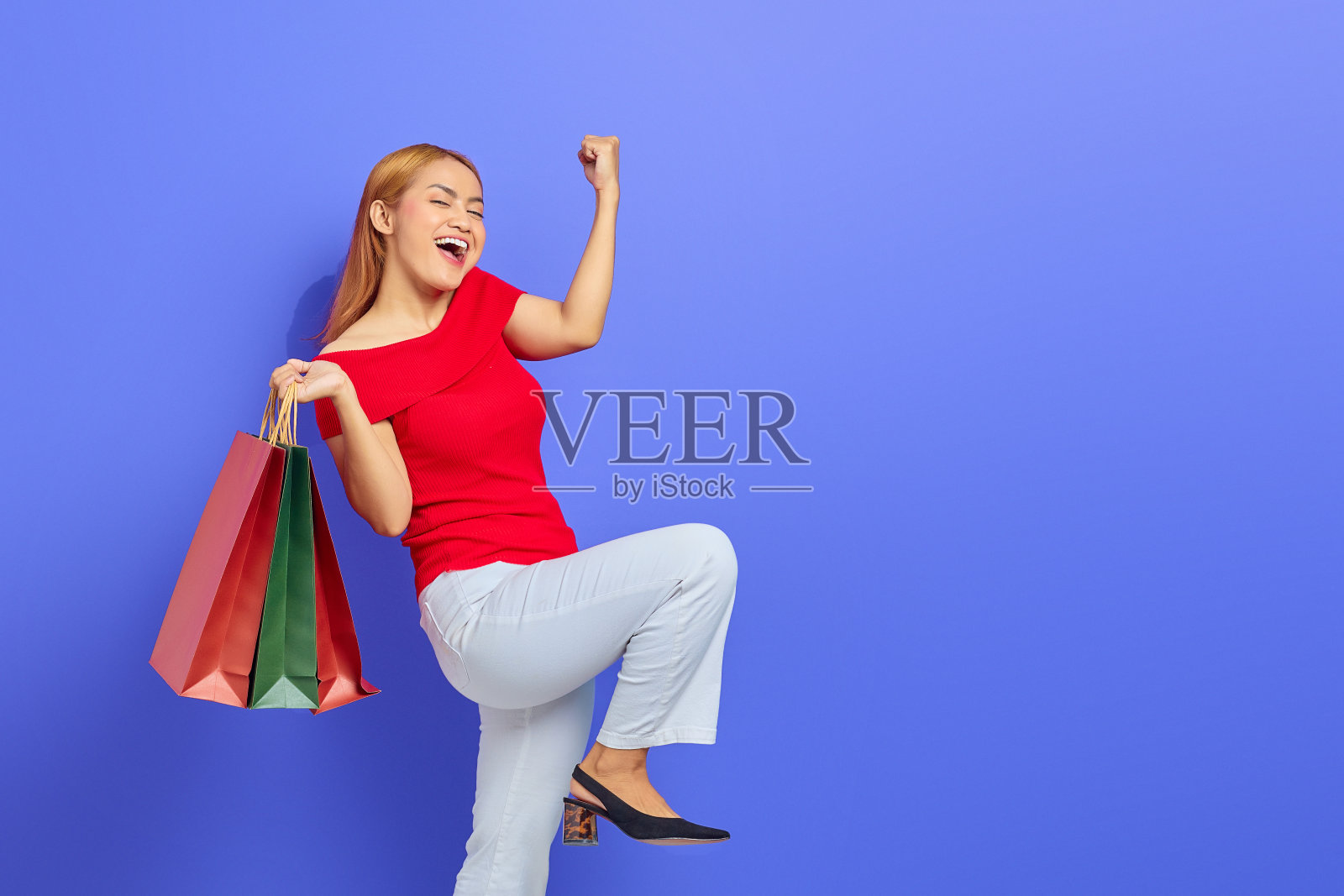 欢快的年轻亚洲女人拿着购物袋和庆祝幸运孤立在紫色的背景照片摄影图片