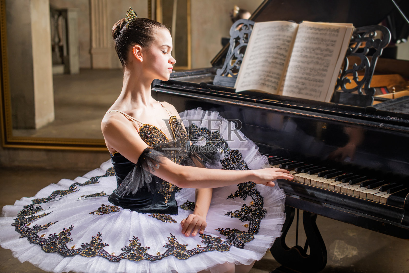 身穿白色芭蕾舞裙的年轻芭蕾舞演员弹奏着一架美丽的旧钢琴照片摄影图片