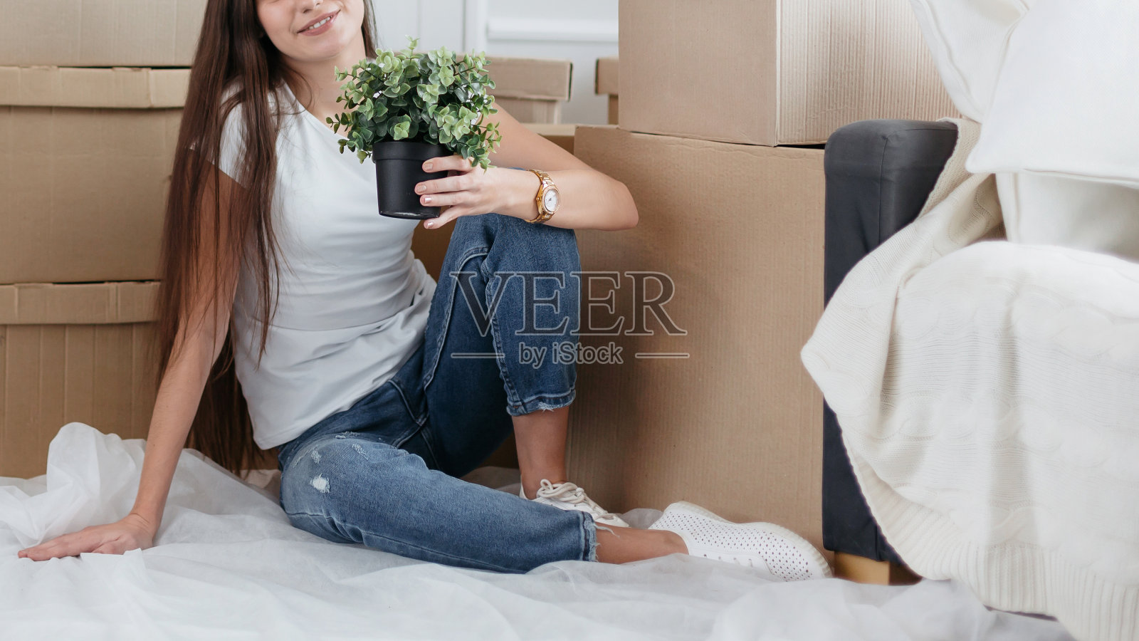 一名年轻女子带着一株家庭植物坐在新大楼的地板上照片摄影图片