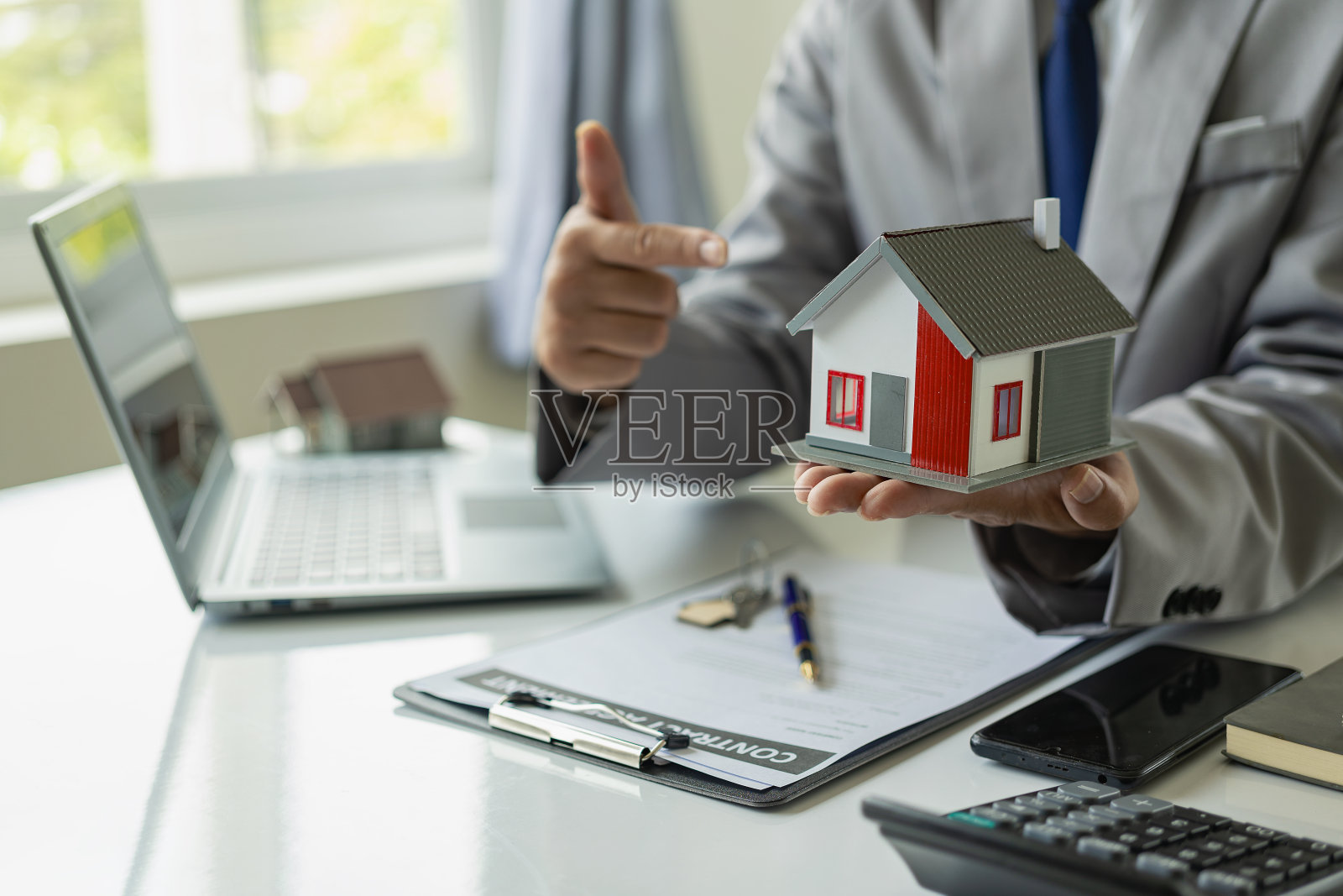 房地产经纪人、保险经纪人、年轻商人和样板房坐在一张桌子上，办公室里有一台笔记本电脑。照片摄影图片