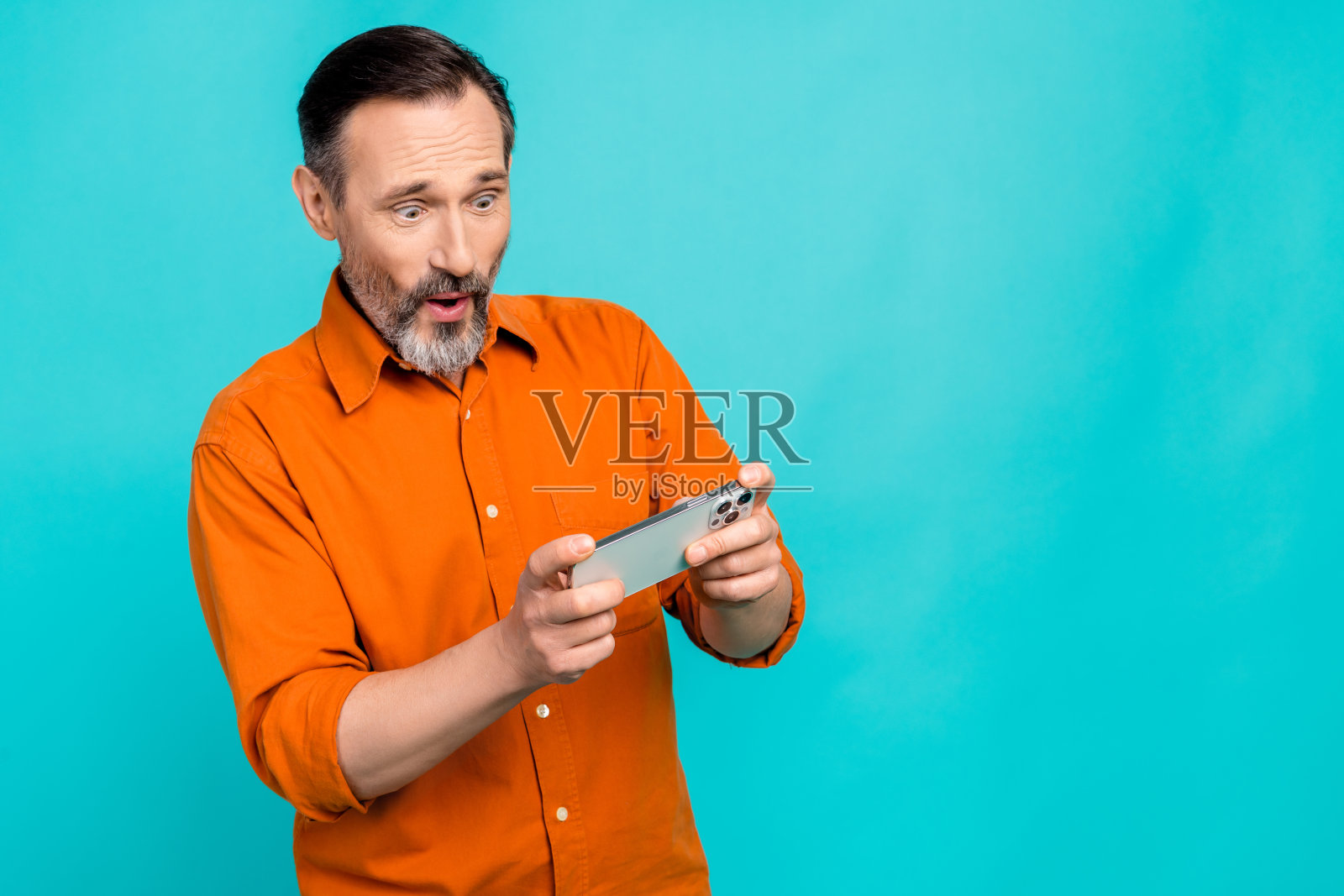 有趣的中年工作企业家拿着手机玩游戏成瘾的照片集中隔离在海蓝宝石色的背景照片摄影图片