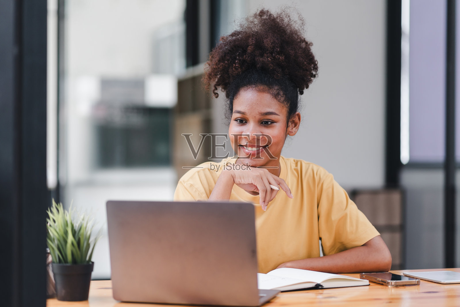 一位年轻的非裔美国妇女在观看网络研讨会视频课程时，正在笔记本上做笔记。非裔美国学生听讲座，通过电子学习在线学习。照片摄影图片