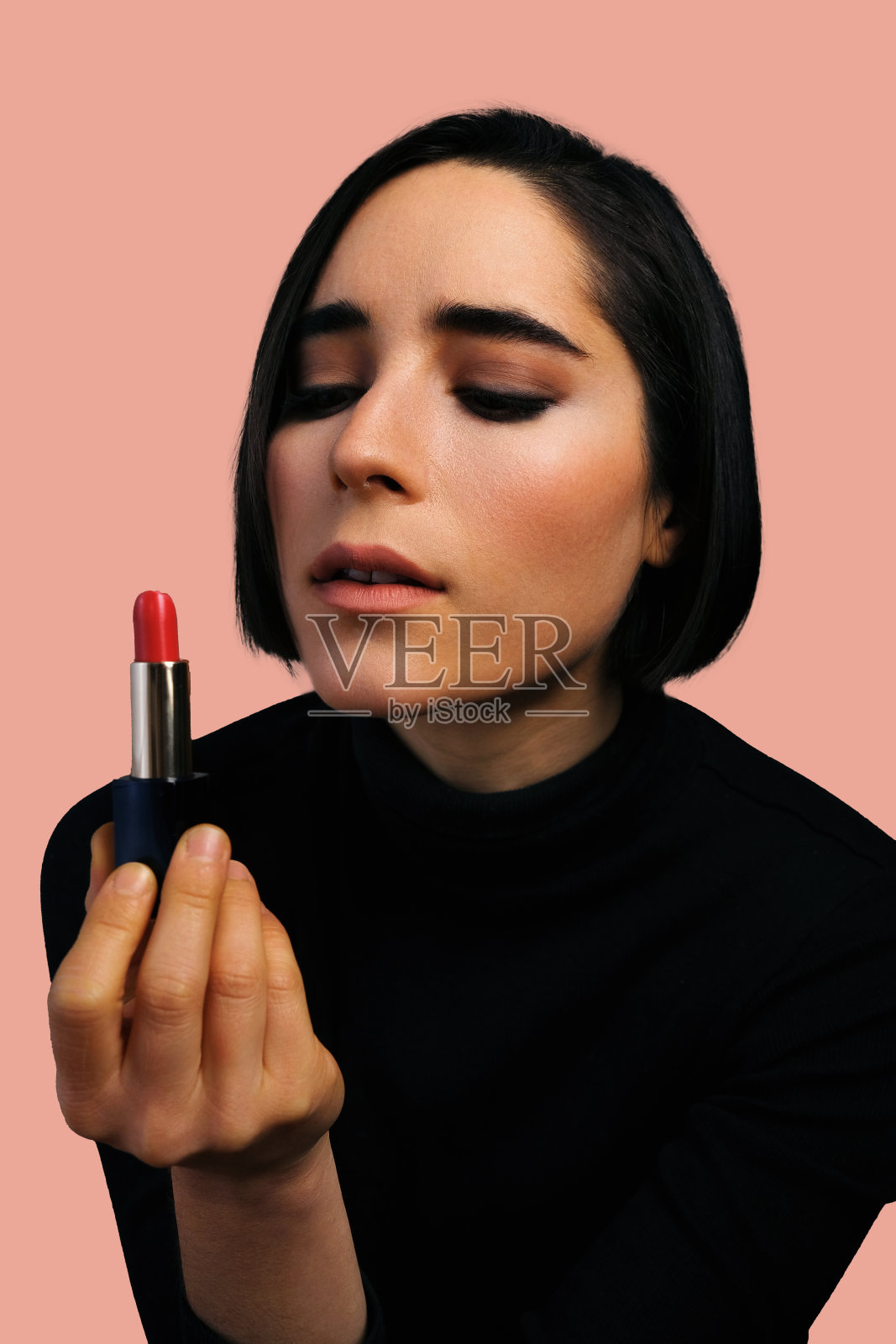 手持红色唇膏的年轻女子在摄影棚拍摄照片摄影图片