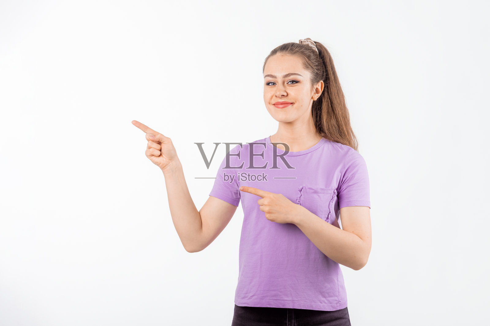 留着长发的年轻女子微笑着指着横幅，一边展示着巨大的促销活动，穿着休闲t恤站在白色背景上照片摄影图片