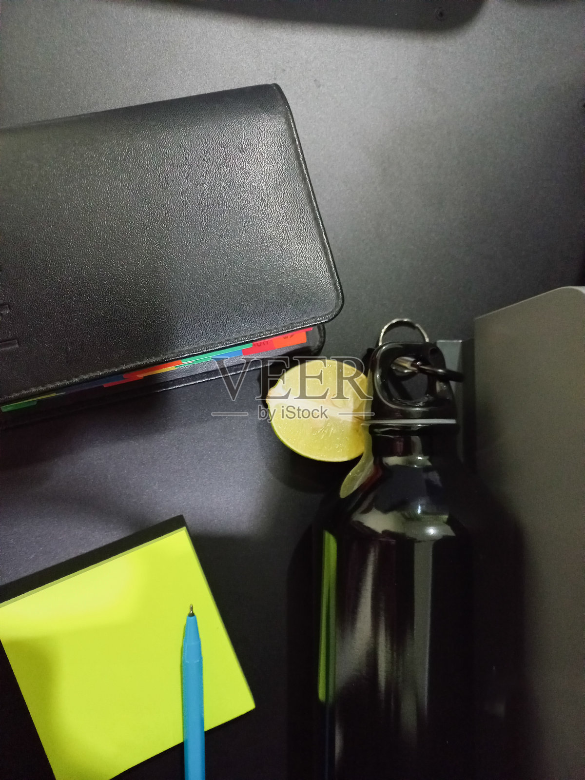 现代黑色办公桌与办公笔记本。日记表。钢笔和黄色的纸贴纸。绿色成熟酸橙和黑色铝运动瓶照片摄影图片