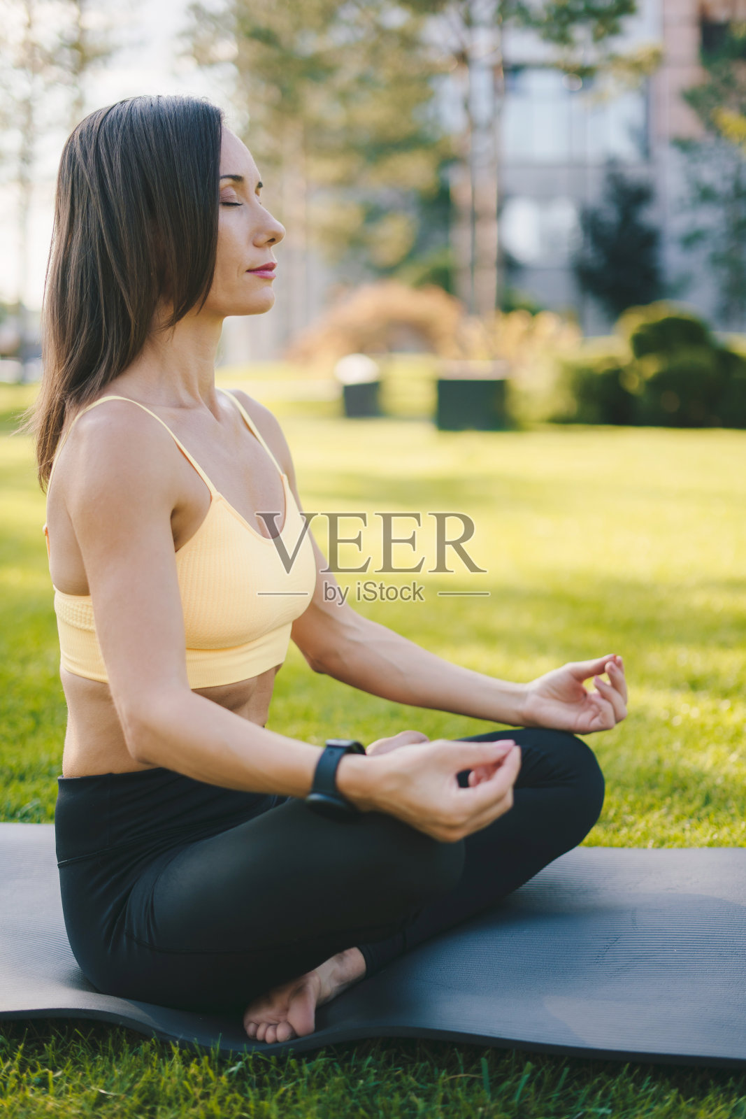 大清早，一个成年女子在绿色公园的瑜伽垫上做瑜伽。健康的生活方式和瑜伽理念。练习瑜伽的女人。健康的生活方式。照片摄影图片