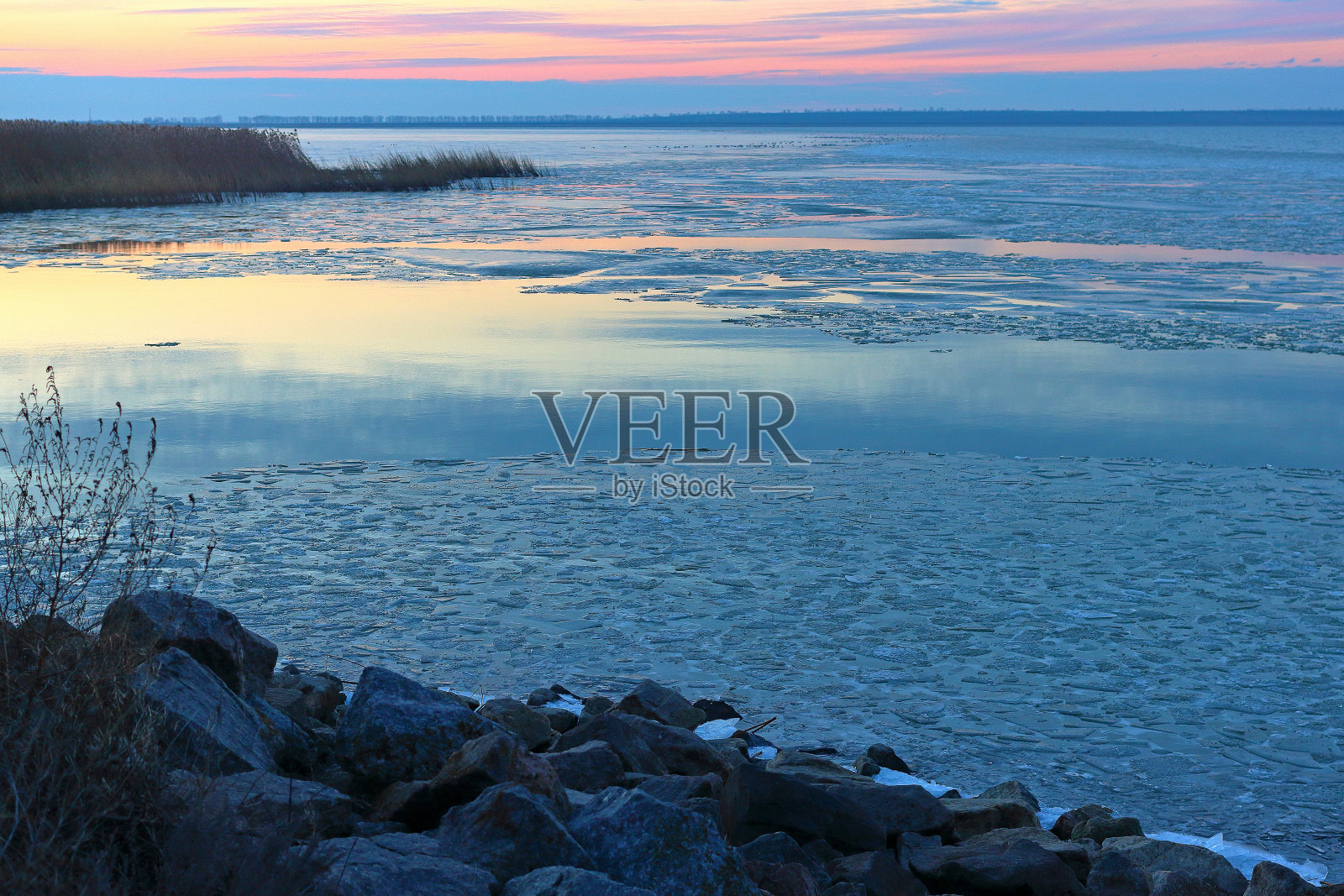 清澈平静的湖面上漂浮着浮冰。湖岸边的花岗岩。蓝色的黄昏的光和紫色的多云的天空在冬天的河流或湖泊照片摄影图片