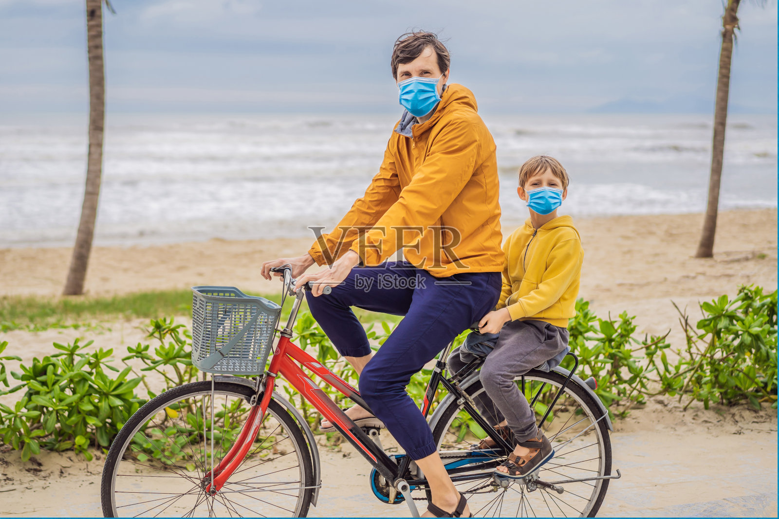 在新冠肺炎期间，父亲带着儿子戴着医用口罩，在美丽的夏日骑着自行车周末远足照片摄影图片
