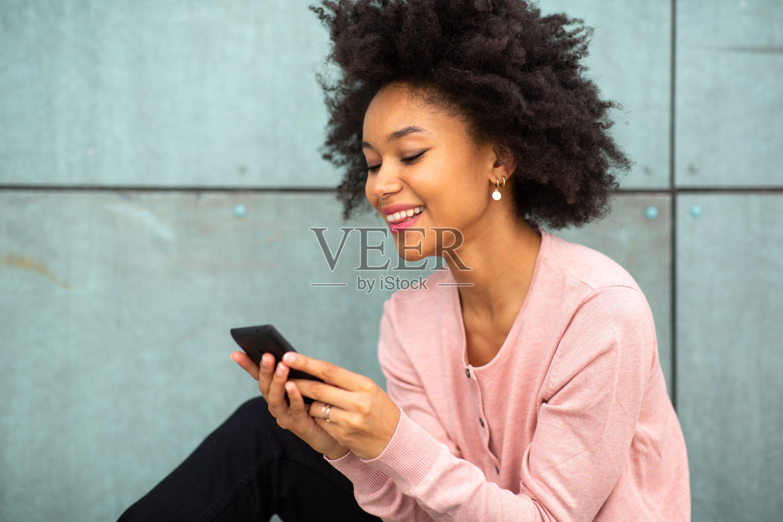 漂亮的年轻黑人女士坐在外面玩手机照片摄影图片