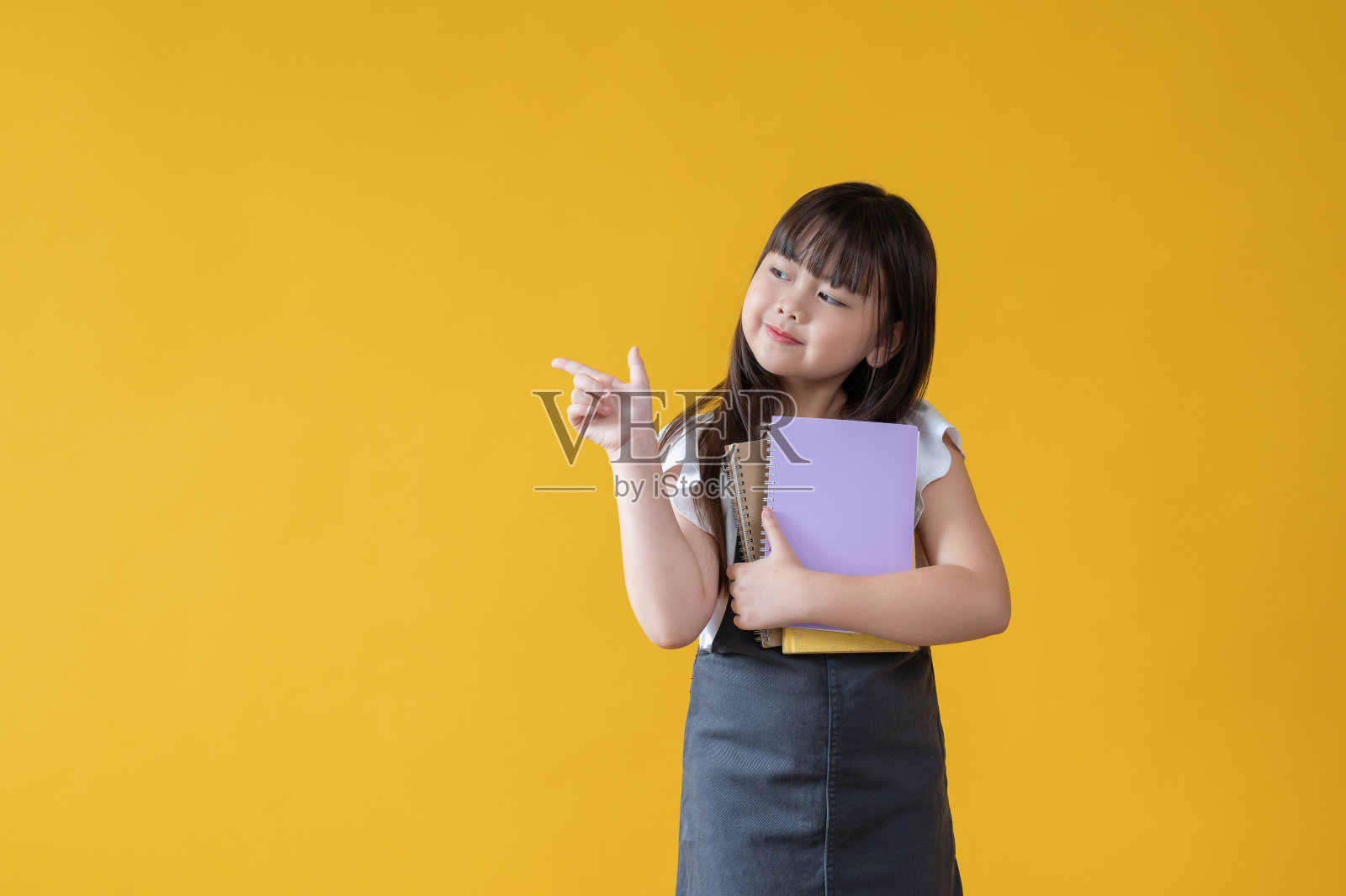 一个可爱的亚洲小女孩拿着书，用手指指着空白的地方照片摄影图片