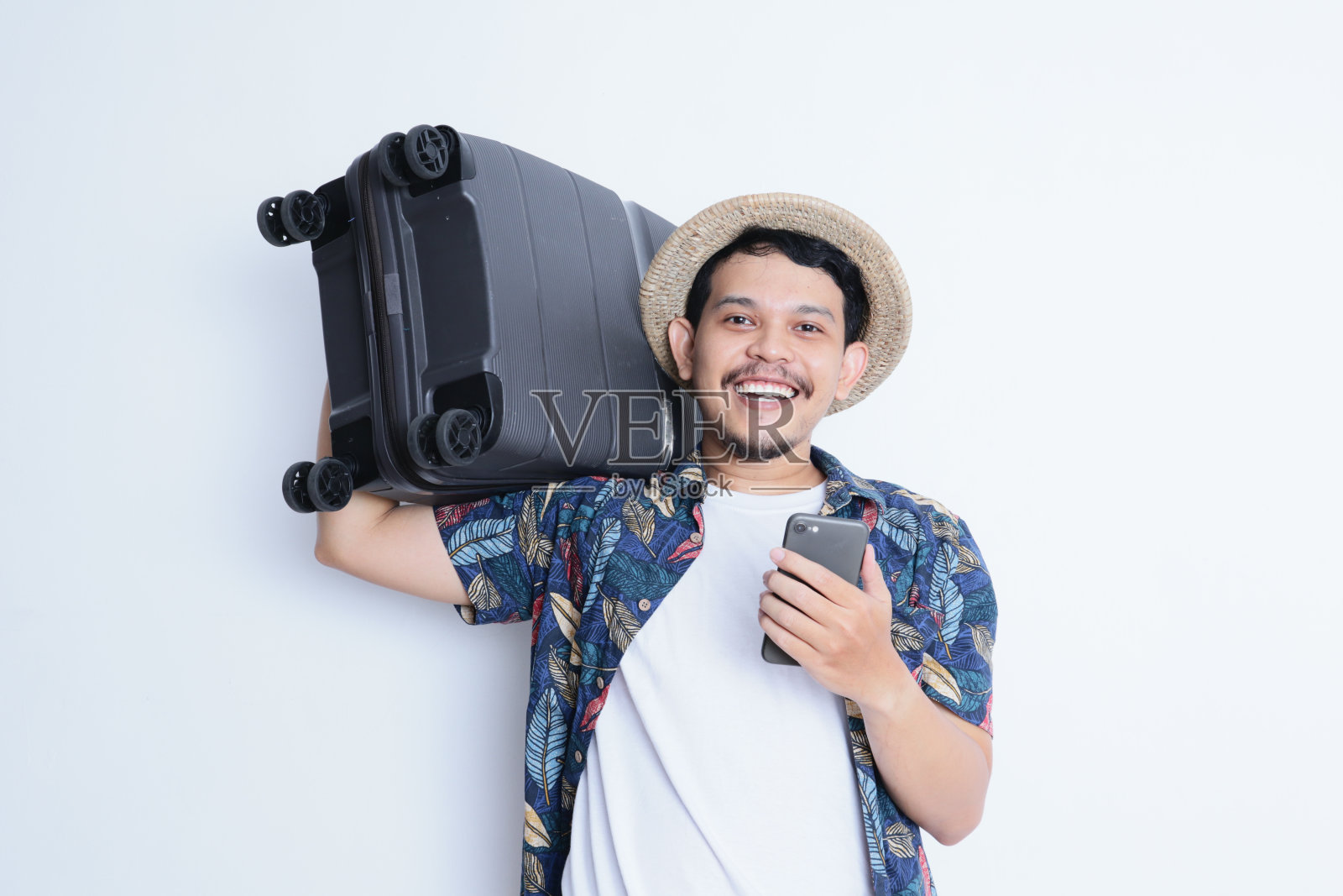 亚洲成年男子带着旅行箱，脸上露出快乐的表情，手里拿着手机照片摄影图片