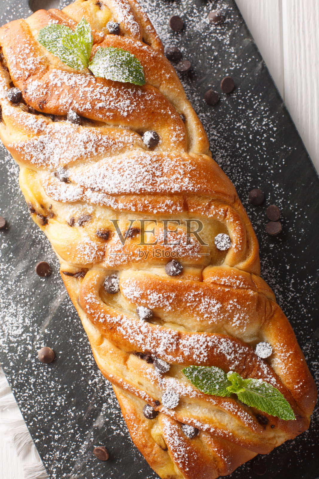 柔软的自制编织甜面包与巧克力和蛋奶冻在桌子上的板板特写。垂直俯视图照片摄影图片