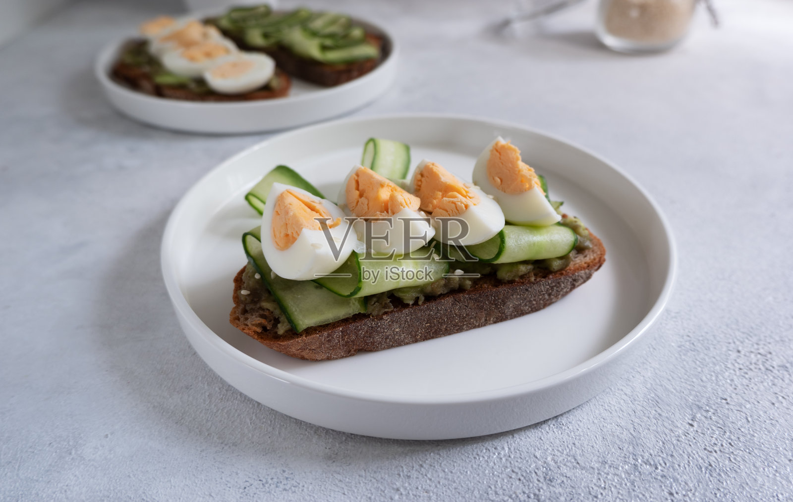 黑麦面包上的牛油果、黄瓜和鸡蛋吐司放在浅色背景的白色盘子里。健康的早餐照片摄影图片