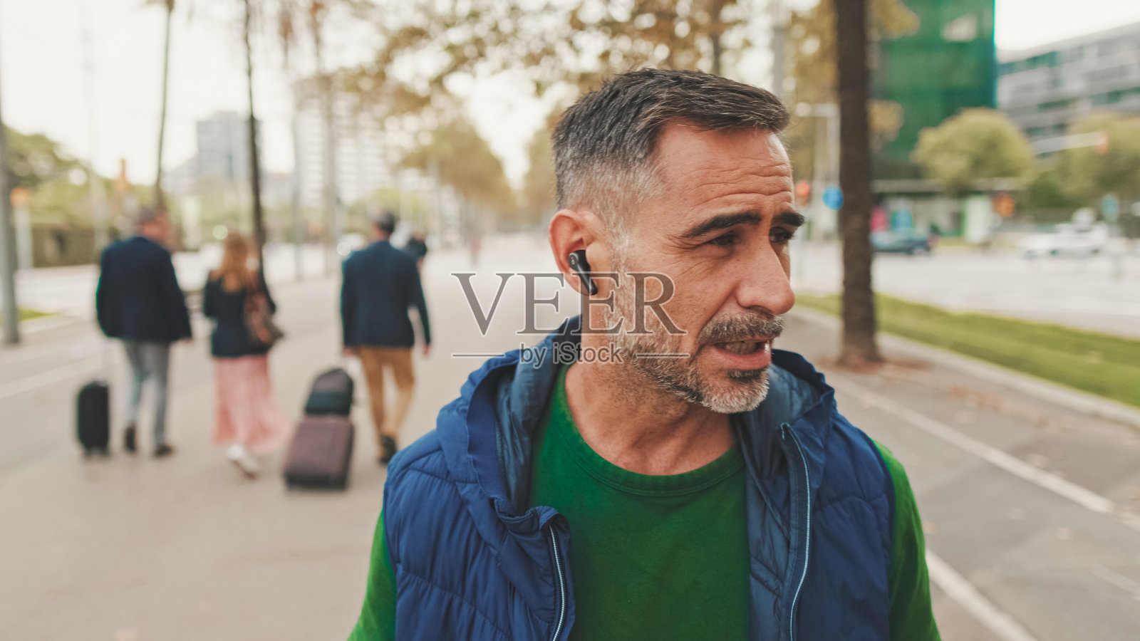 穿着便服的成熟男子在广场上行走时戴着耳机、无线耳机说话照片摄影图片