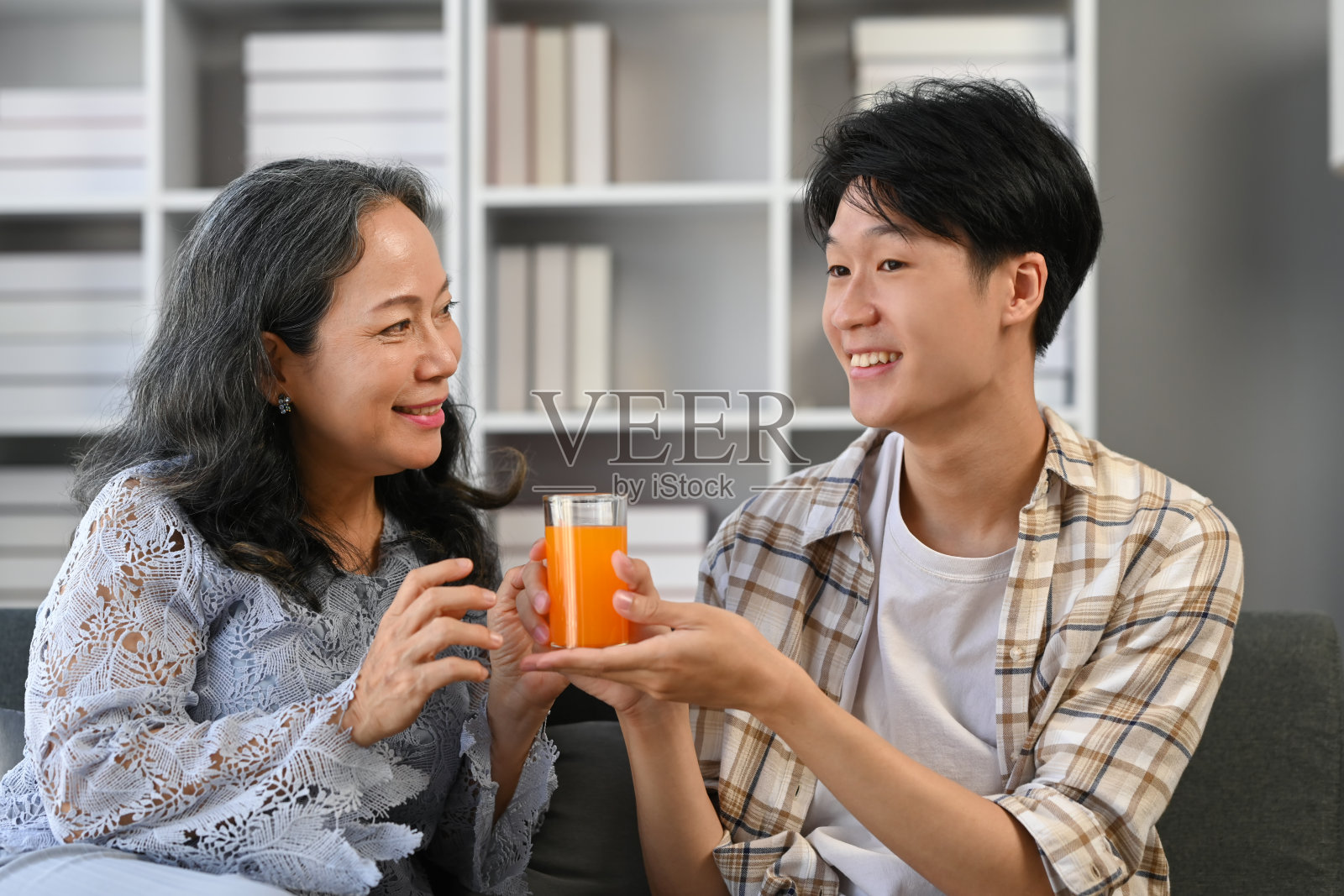 慈爱的成年亚洲男子坐在客厅里给祖母一杯橙汁。照片摄影图片