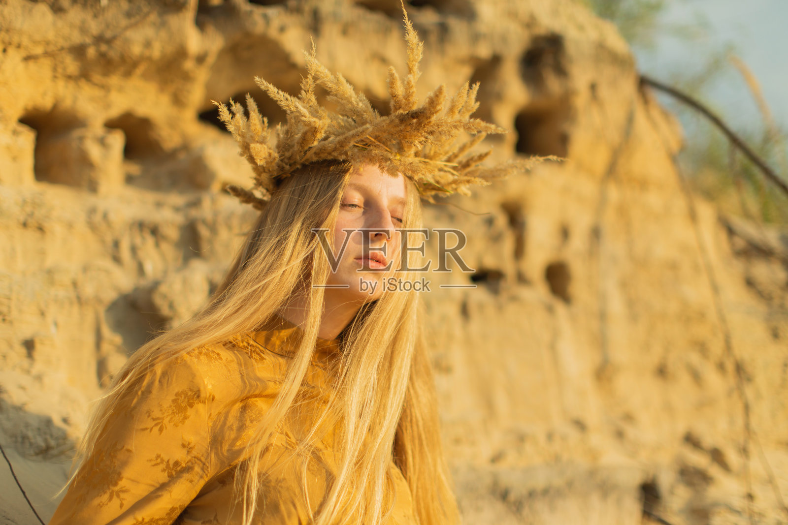 穿黄色衣服的金发女子用干草编织花环。夏天的一天。长头发的。沙子。照片摄影图片