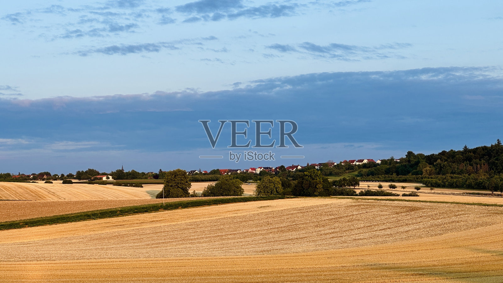 夕阳下收获的麦田，山脊上的村庄照片摄影图片