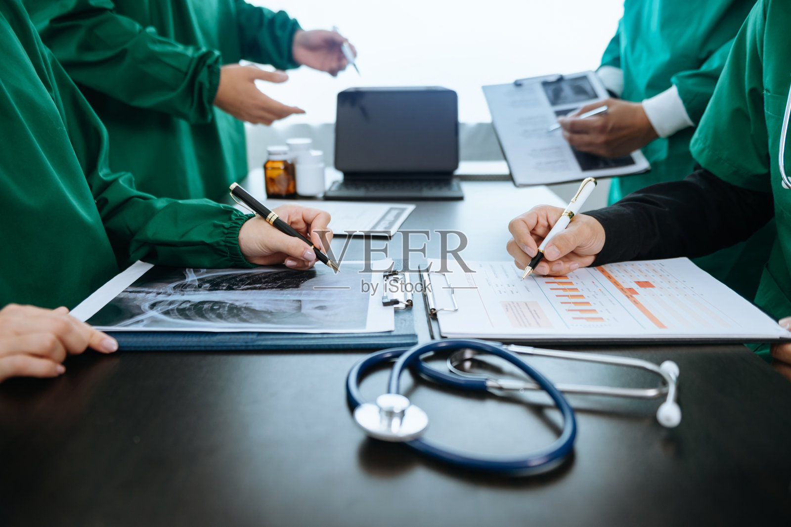 医疗团队正在开会，穿着白大褂和外科手术服的医生坐在桌子旁，讨论医疗行业中使用计算机在线工作的患者照片摄影图片