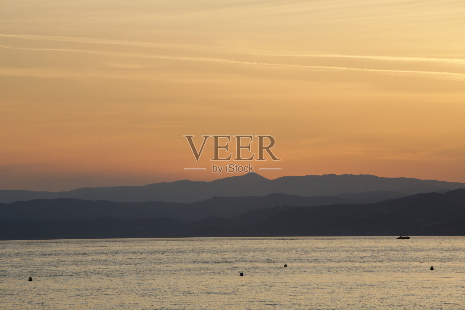 在充满活力的橙色日落时，静止的海水后面的山层剪影照片摄影图片