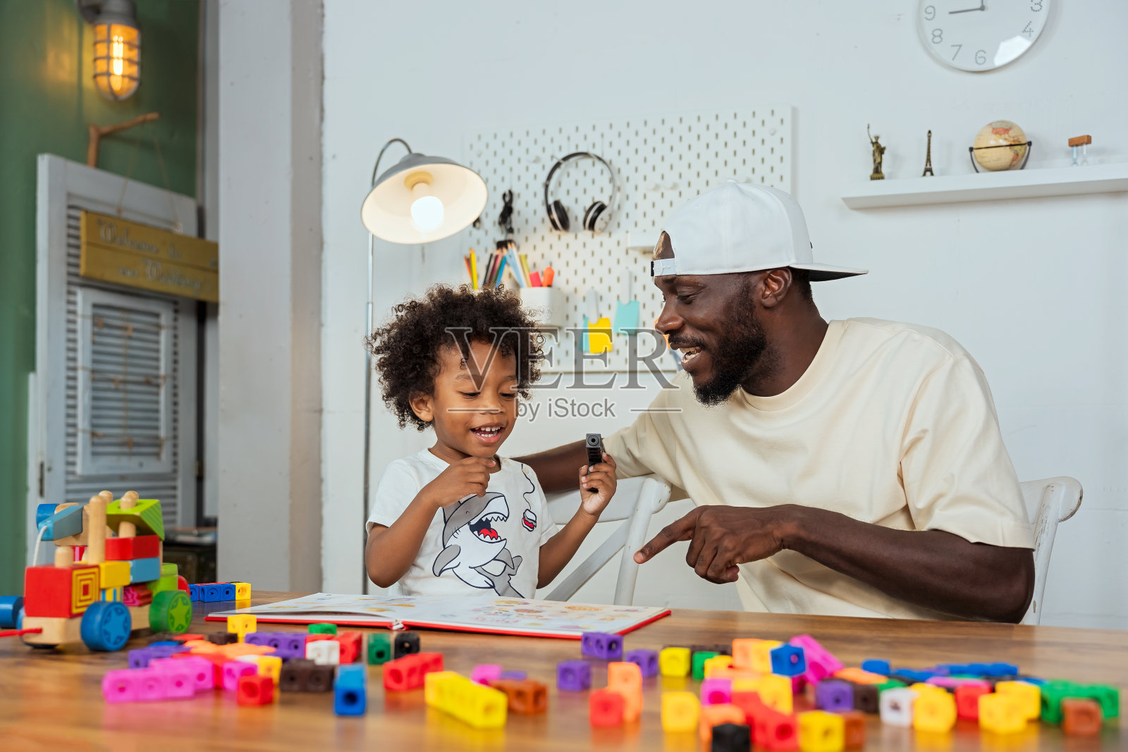 一位黑人父亲教他的儿子如何阅读，并看着他的孩子玩拼图游戏，以提高孩子的学习技能。提高学习技能的学习材料。照片摄影图片