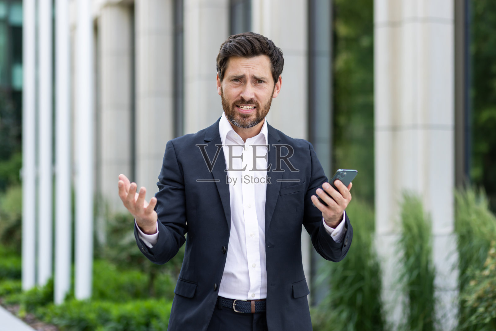 沮丧和失望的年轻商人，律师站在办公室外，拿着电话，摊开双手看着镜头照片摄影图片