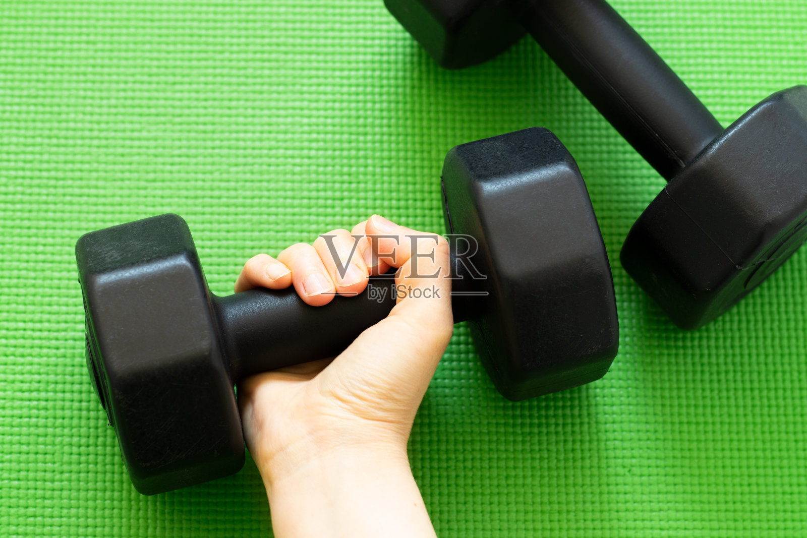 女性的手握哑铃在绿色的训练垫背景照片摄影图片