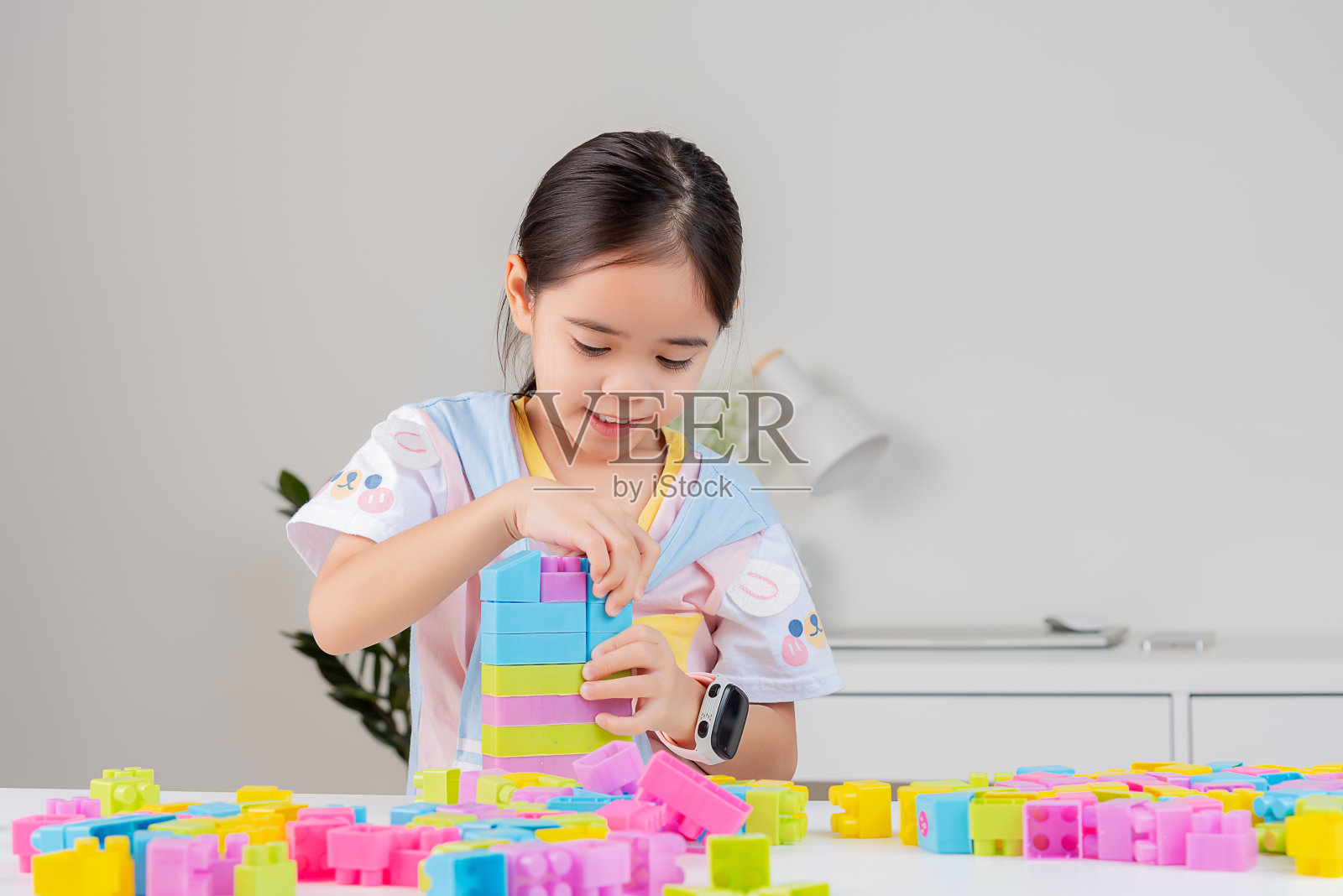 小女孩正在玩五颜六色的积木拼图。在白色的房间里照片摄影图片