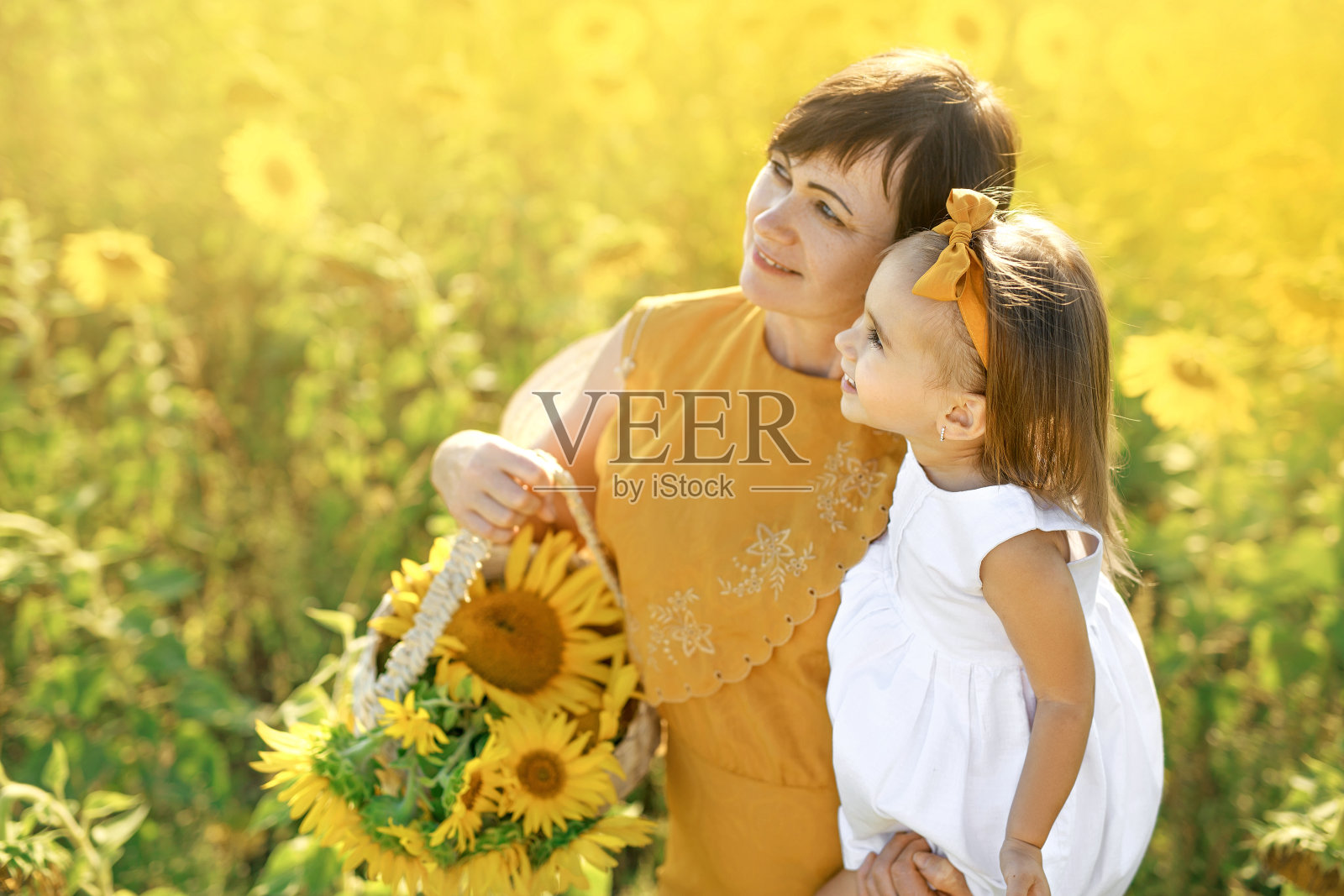 快乐的祖母和孙子看着拷贝空间。自然背景。老妇人抱着花篮，怀里抱着孩子。假日和散步在新鲜的空气在日落。在一起的幸福照片摄影图片