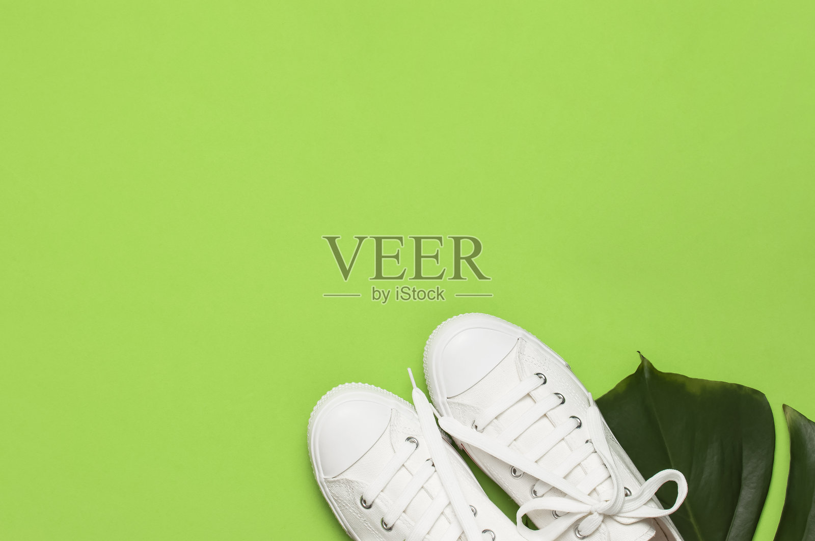 白色女性时尚运动鞋，热带树叶在绿色背景。平面俯视图拷贝空间。女性的鞋子,配饰。时尚的白色运动鞋。夏天创意概念照片摄影图片