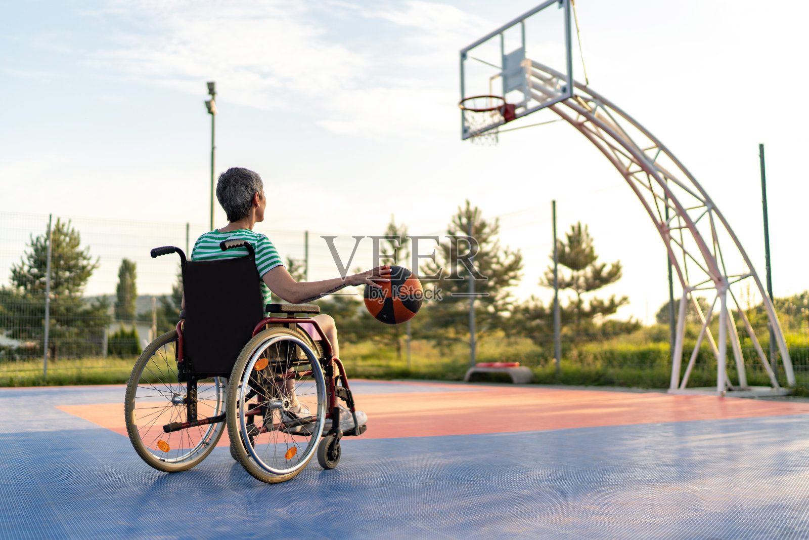 坐在轮椅上的老年妇女在室外篮球场投篮照片摄影图片