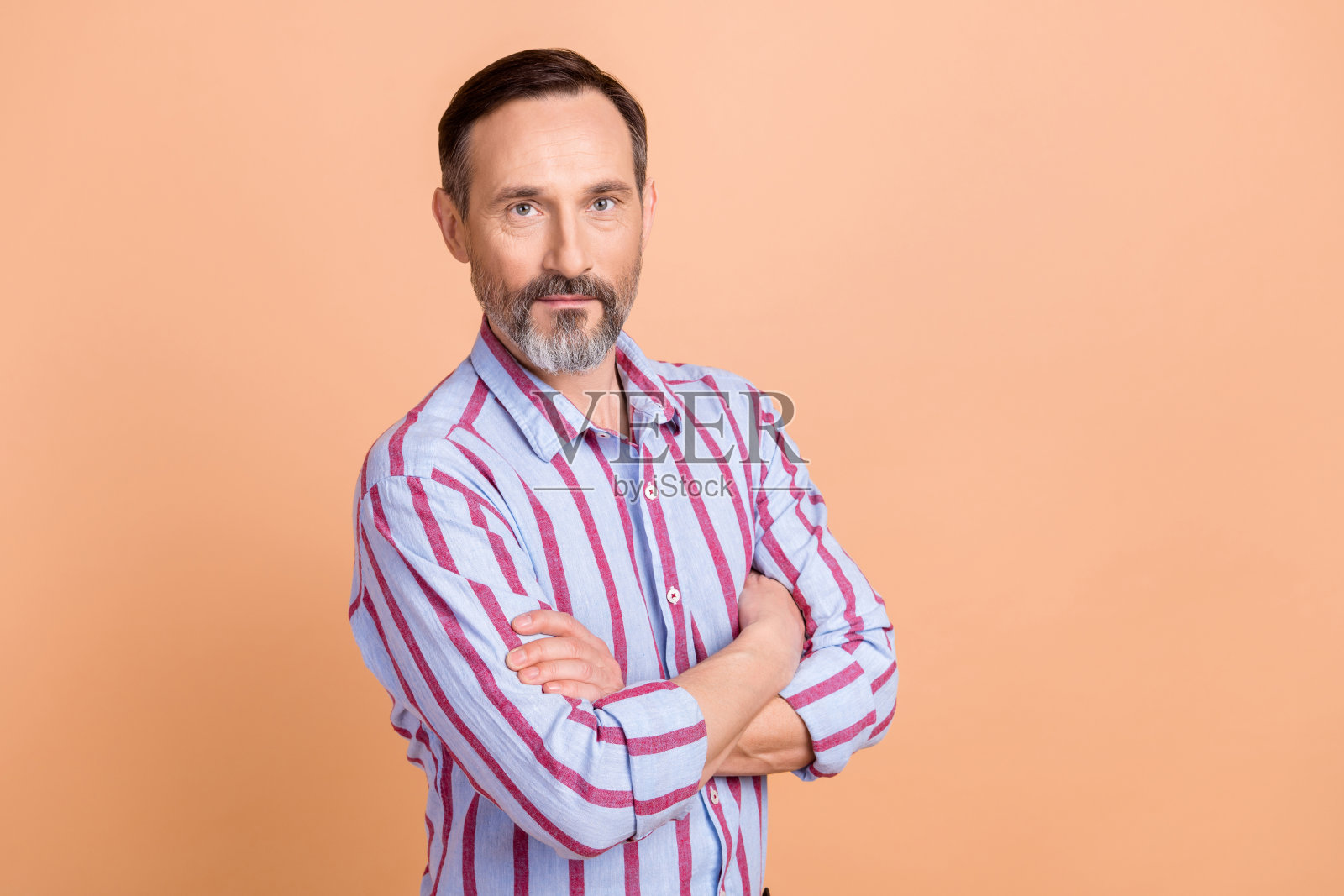 照片英俊的好心情的男人与灰色的胡子穿着条纹正装衬衫，双手交叉孤立的米色背景照片摄影图片