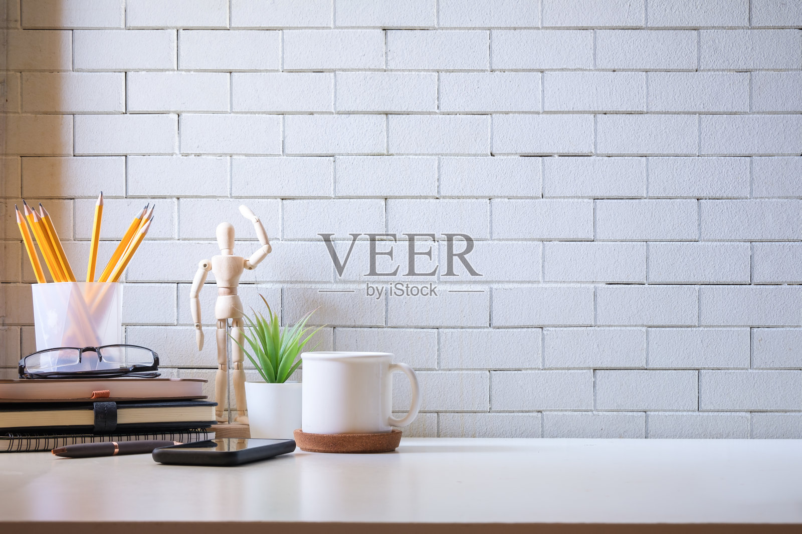 时尚的工作空间，白色的桌子上有咖啡、书、室内植物和铅笔架。照片摄影图片